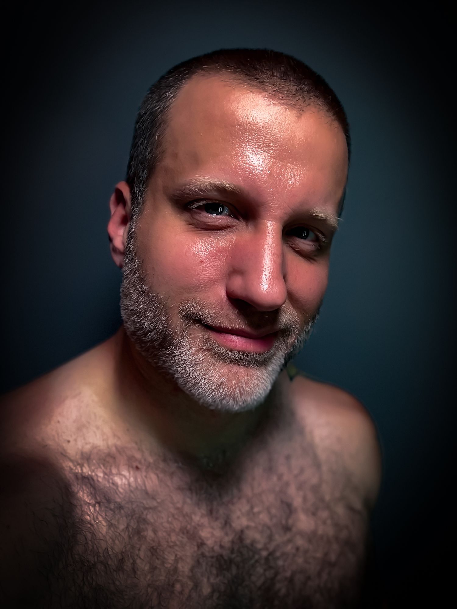 Portrait of a bearded person smiling against a dark blue background.