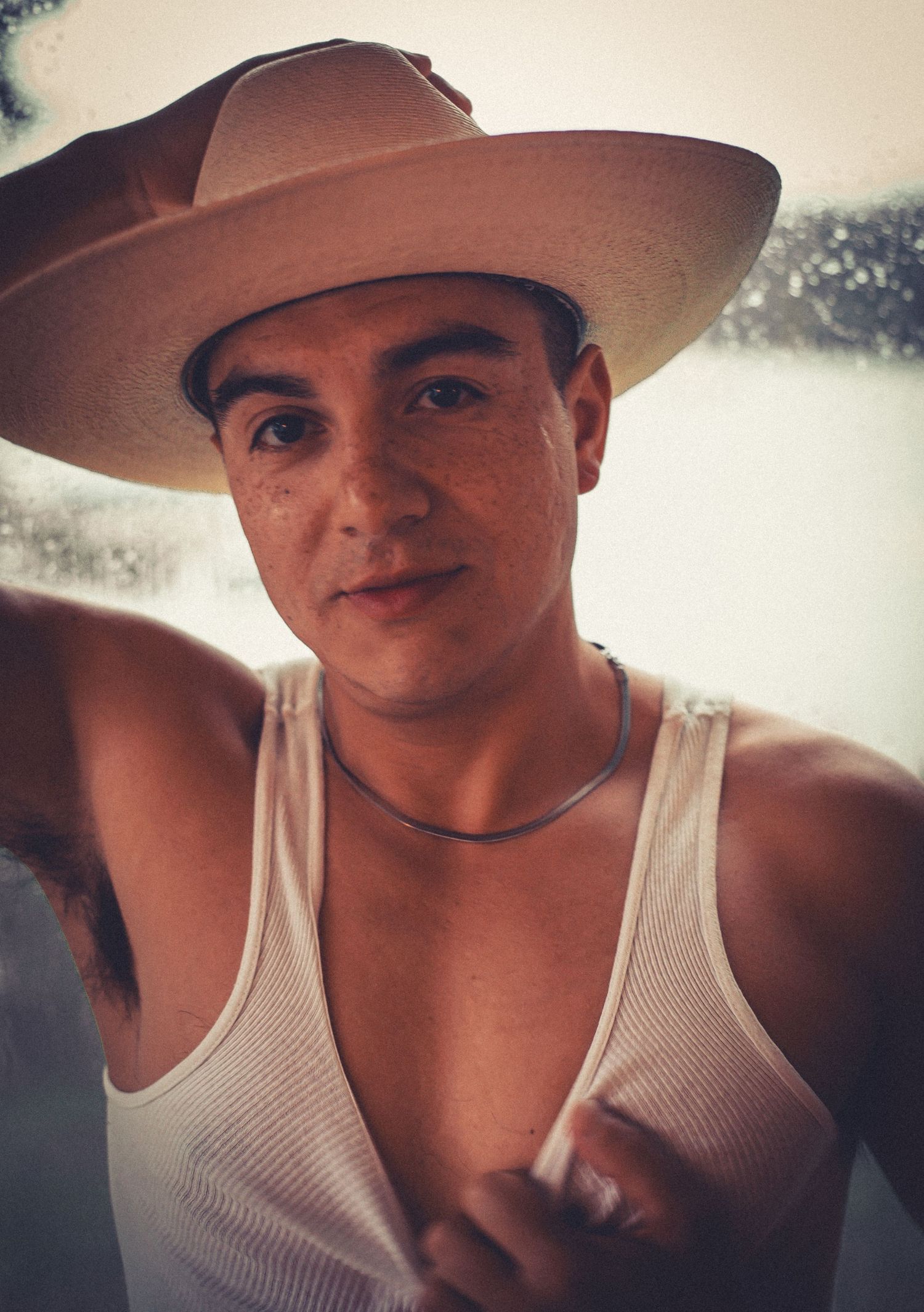 Portrait of someone wearing a cowboy hat and white tank top.