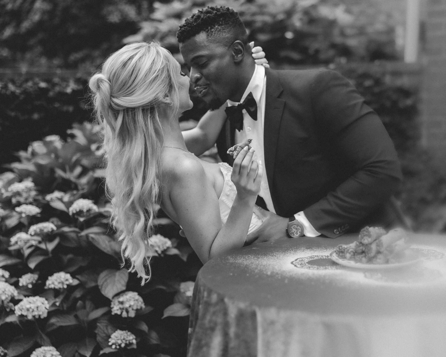 A romantic black and white photo series of a couple embracing among flowering hydrangea bushes in a garden setting.