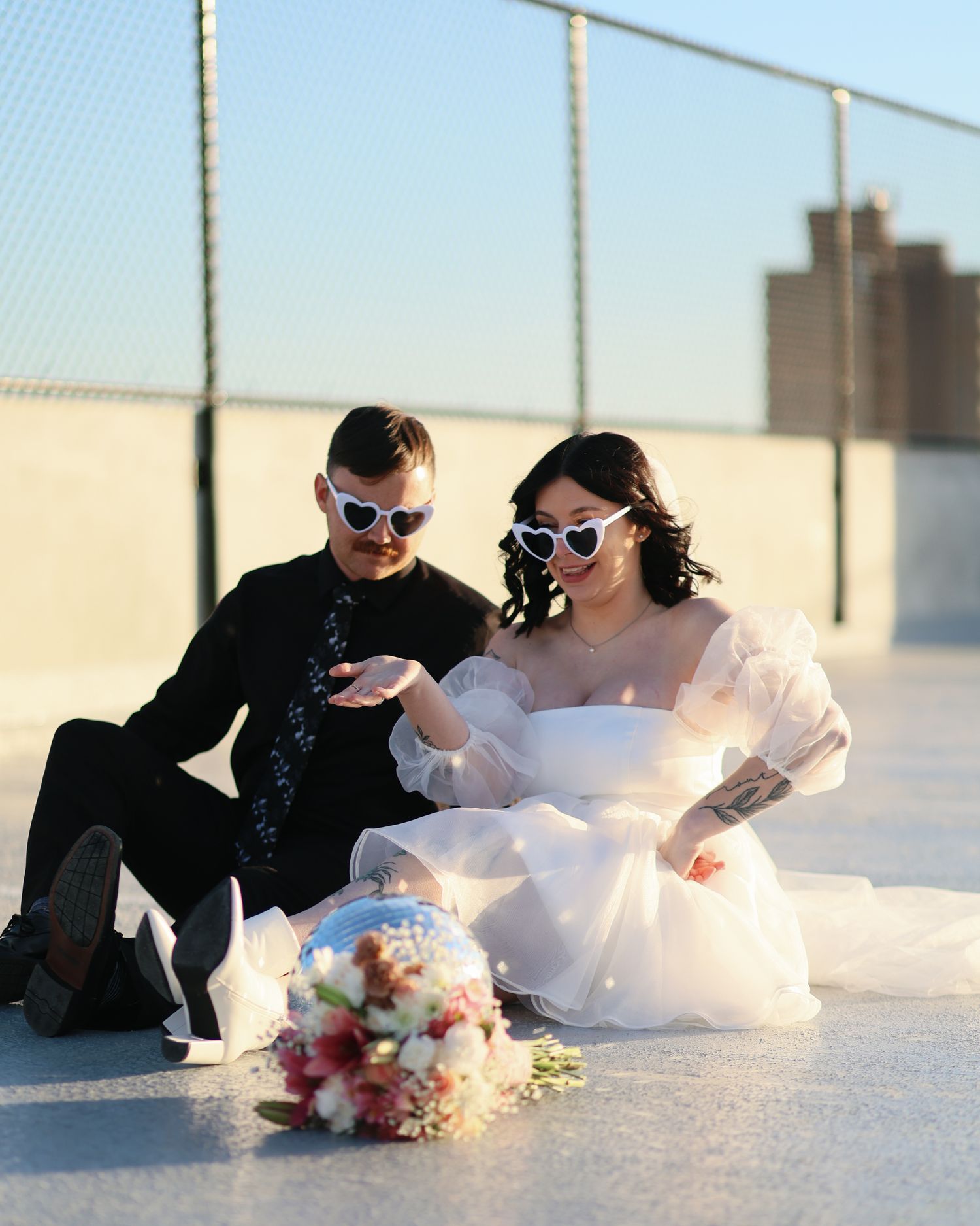 A couple in wedding attire playfully poses on the ground in a series of connected photos at sunset.
