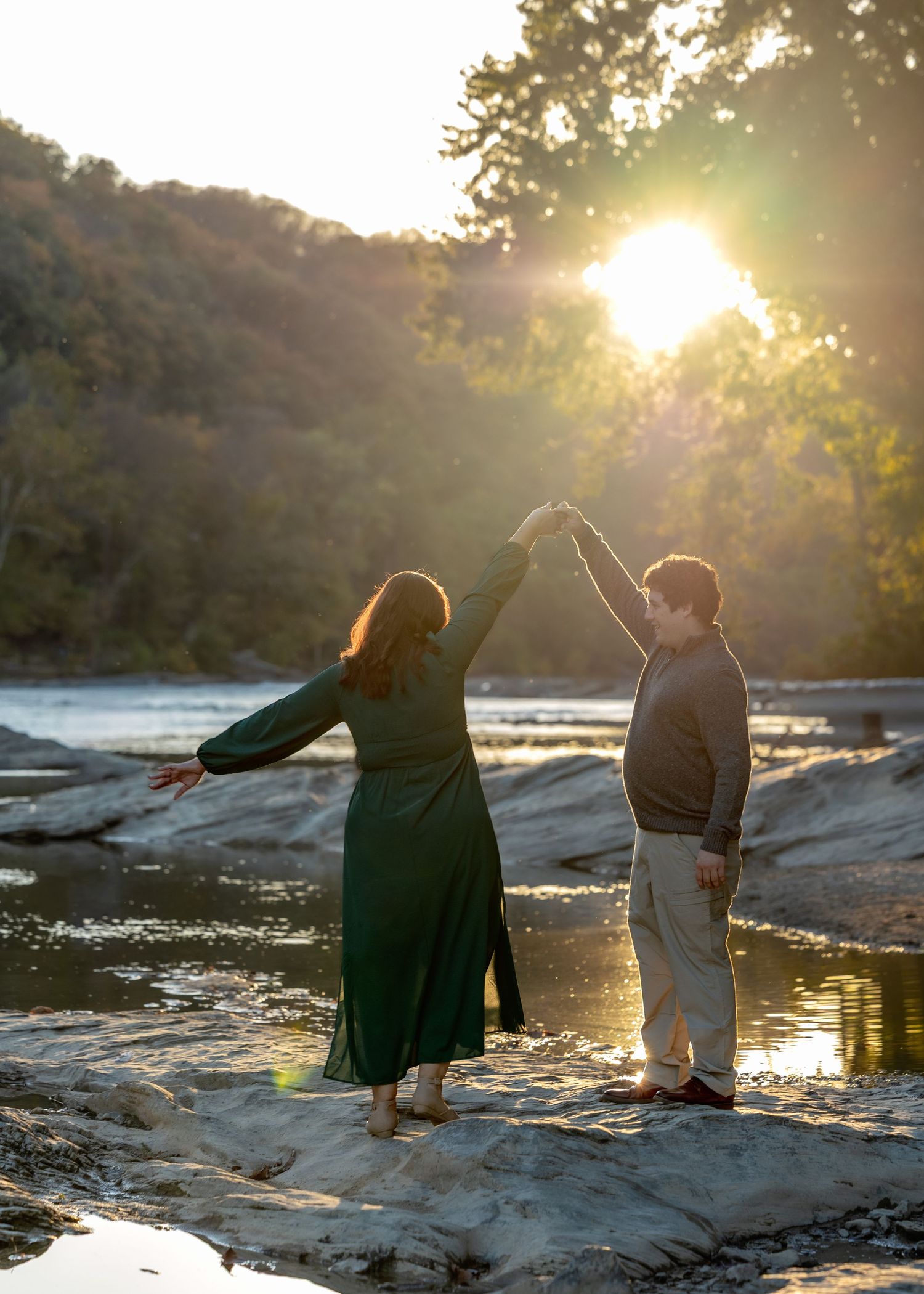 Two people sit on rocks by a serene lake at sunset, creating a peaceful silhouette against the golden light.