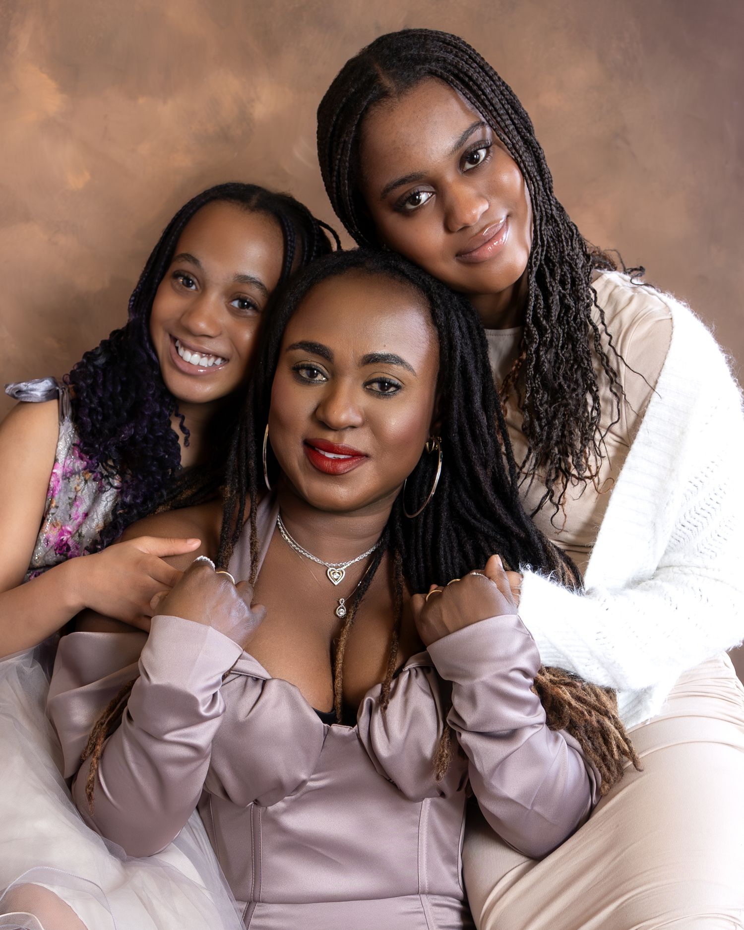 A woman and two girls pose together in a professional studio portrait with warm brown backdrop.