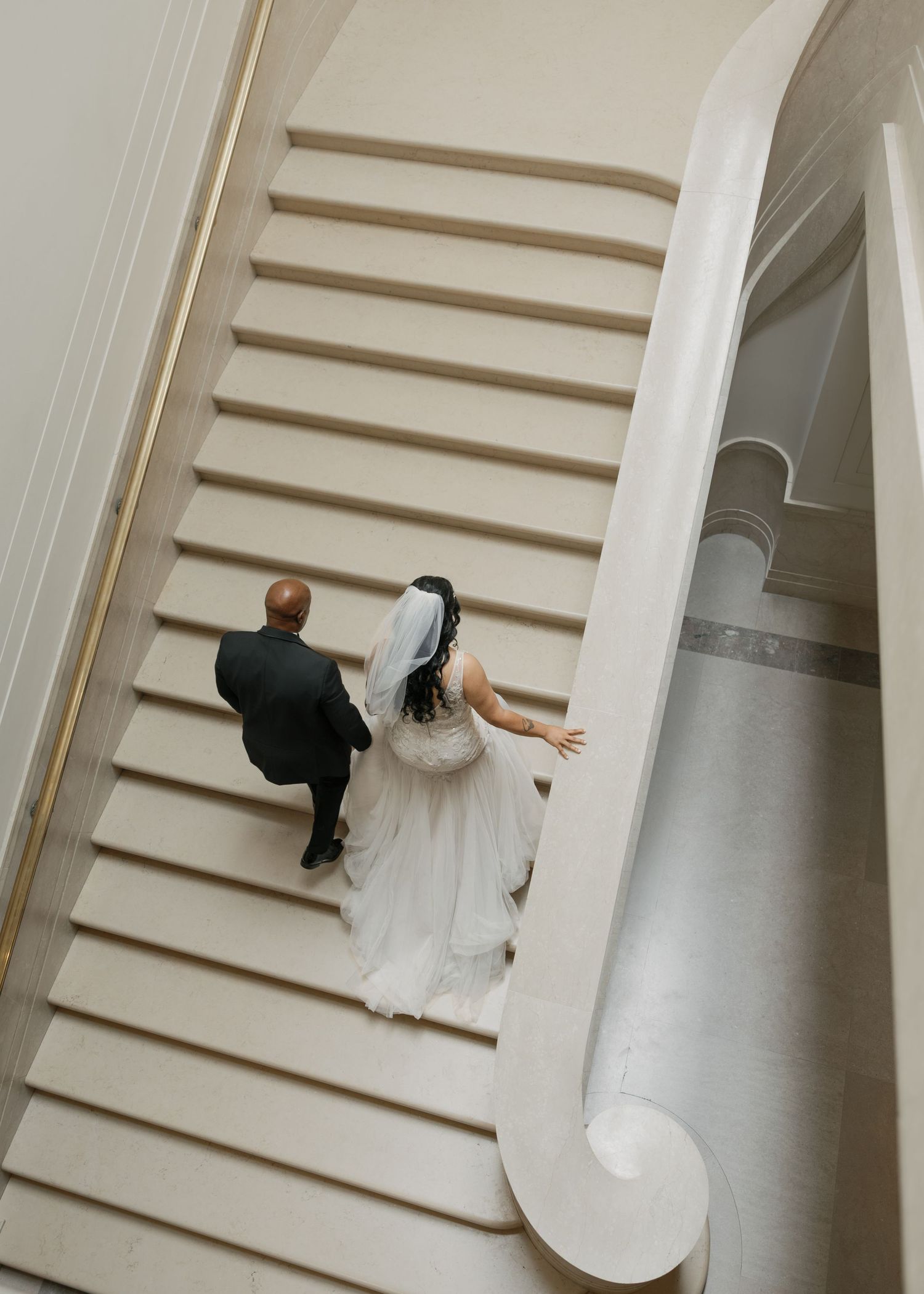 Aerial view of bride and groom walking up elegant white staircase on their wedding day.