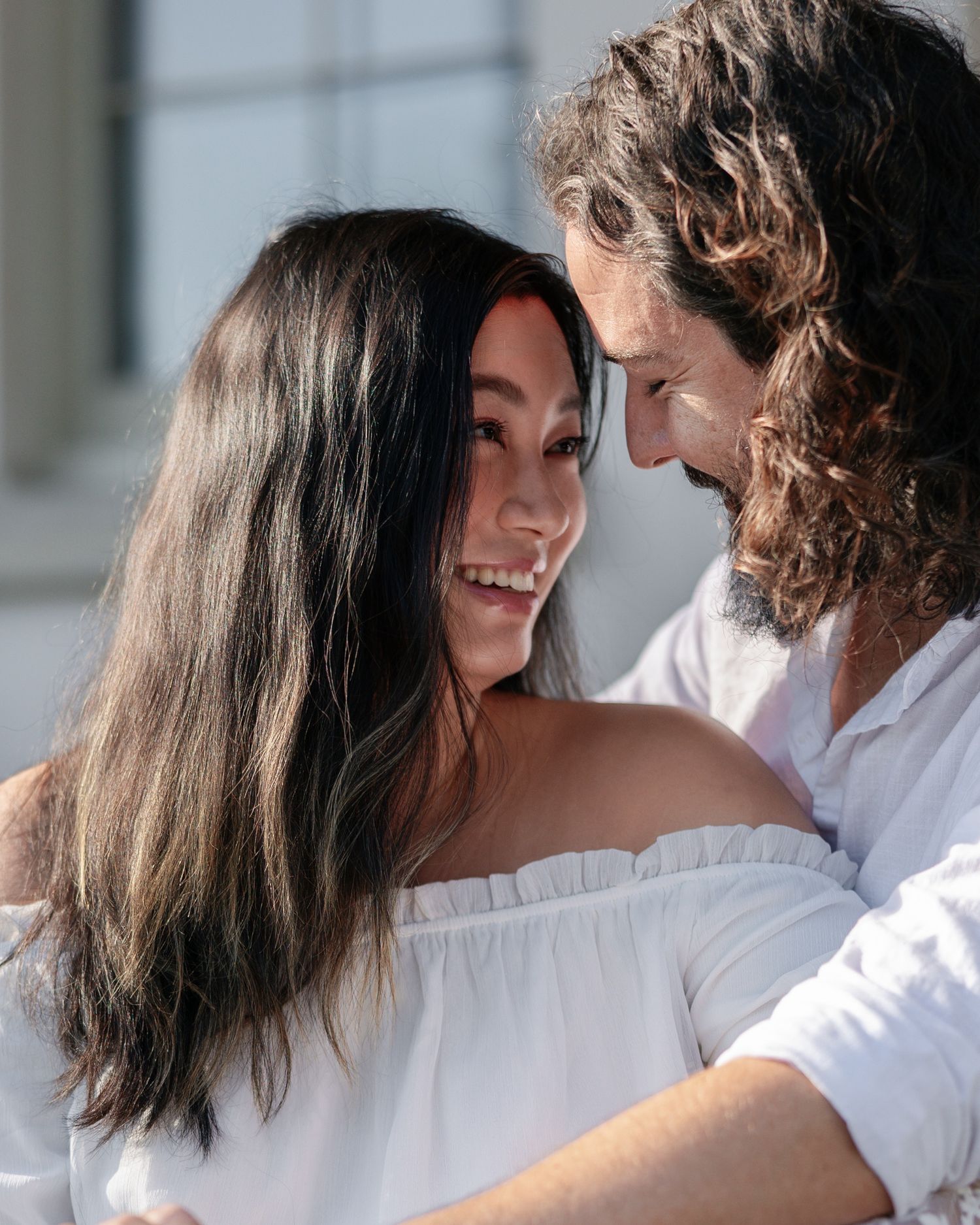 A romantic couple in white outfits share an intimate moment together while smiling and embracing.