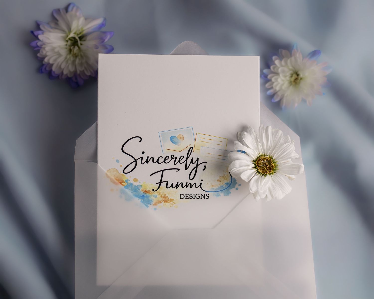 Sincerely Funmi Designs logo on white card in envelope with white daisy and blue flowers on satin.