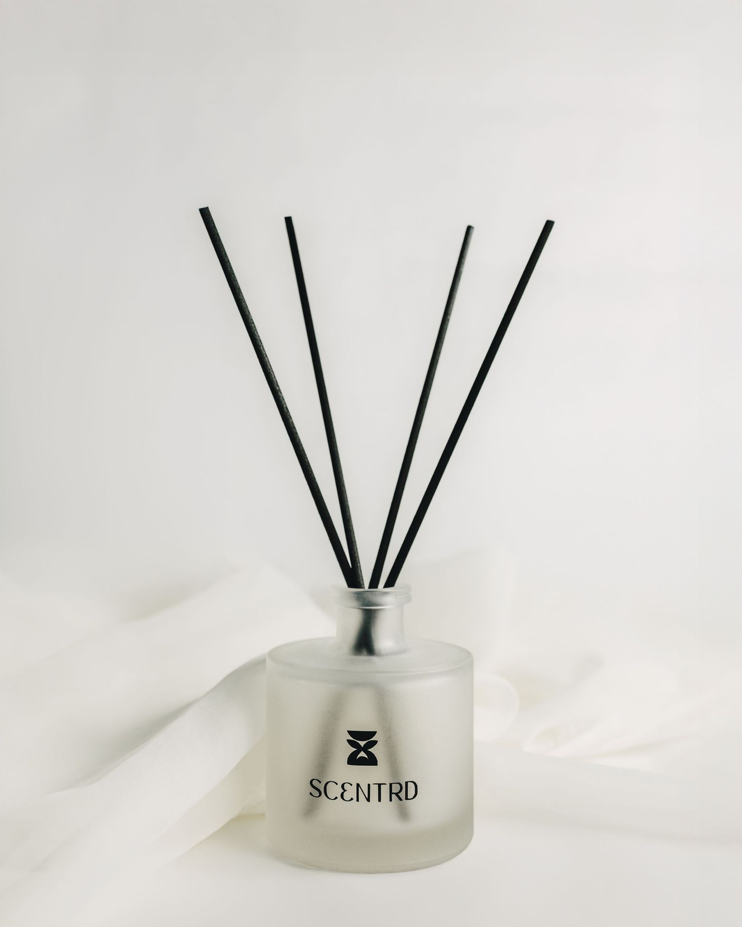 Frosted glass reed diffuser by Scentrd with black reeds on white background.