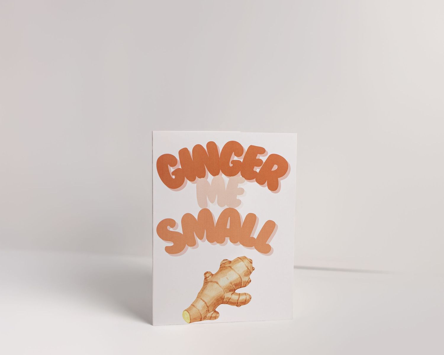 White greeting card with bold orange bubble letters reading Ginger Me Small with an illustrated ginger root below.