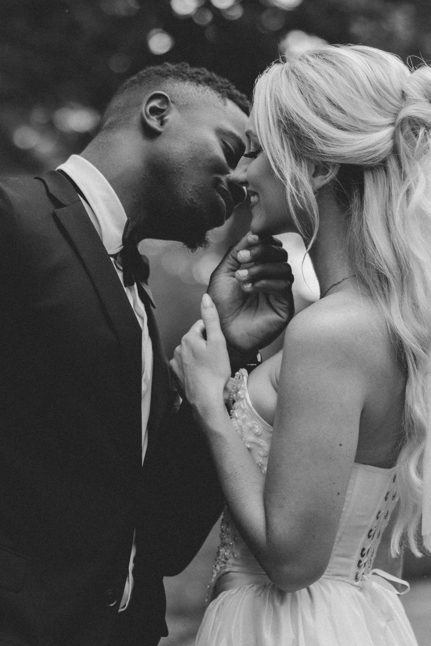 Black and white wedding photo of a romantic intimate moment between newlyweds in formal attire outdoors.