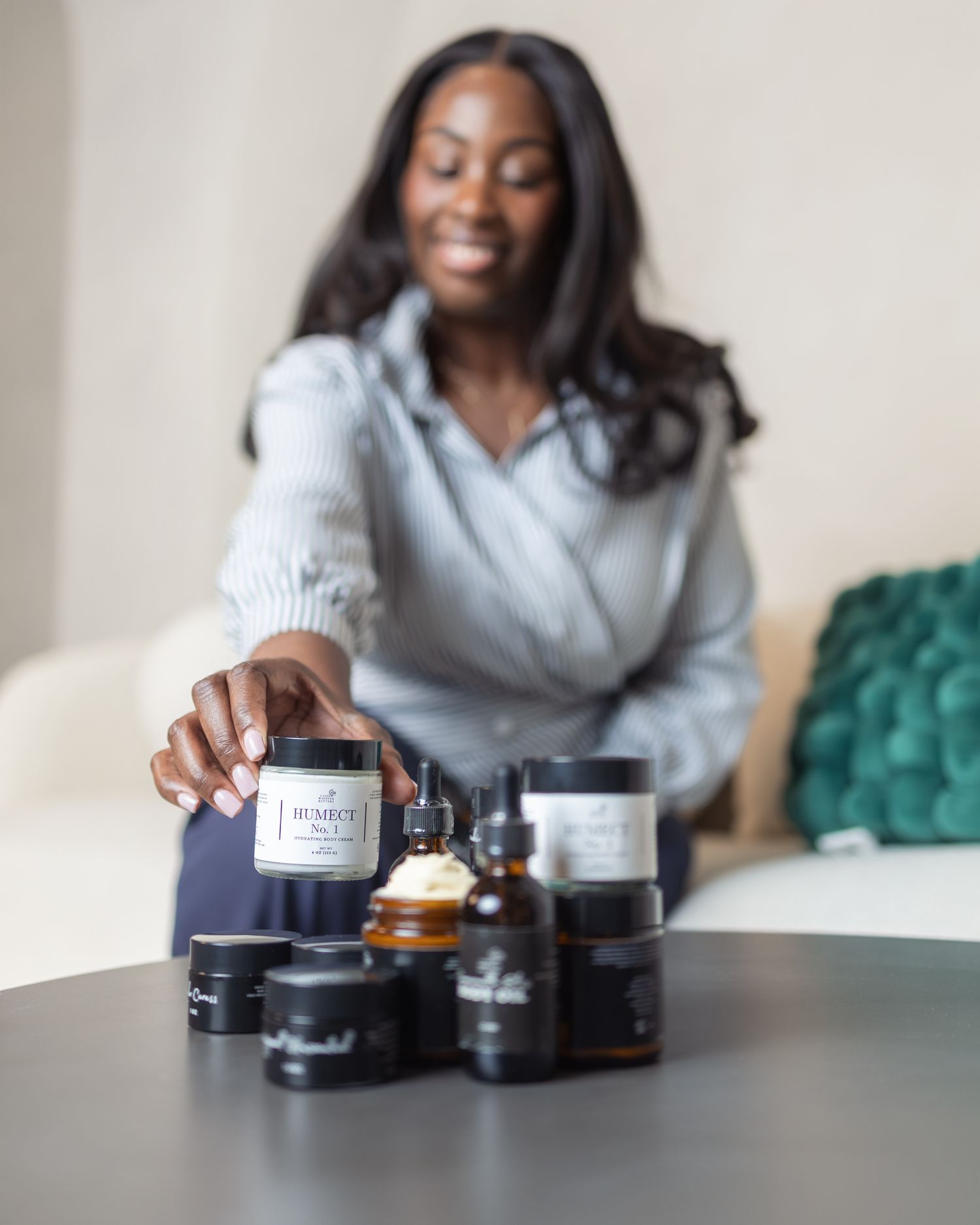 Woman smiling while arranging skincare products including serums and creams on a dark table.