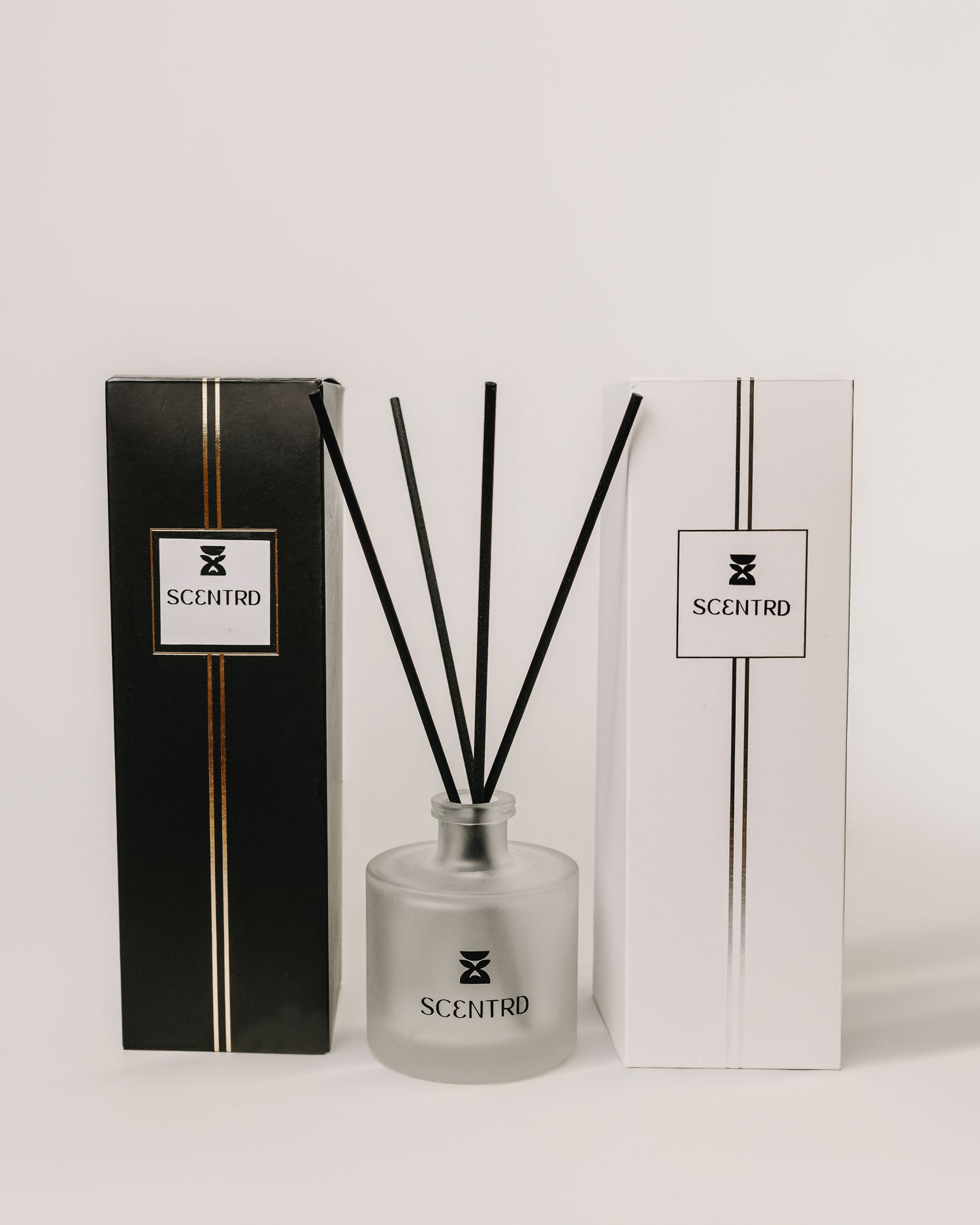Scentrd reed diffuser in frosted glass bottle with black reeds, displayed between black and white branded gift boxes.