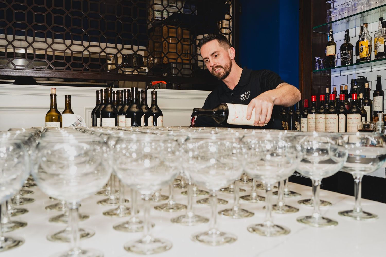 Row of empty wine glasses lined up on a dark bar counter.