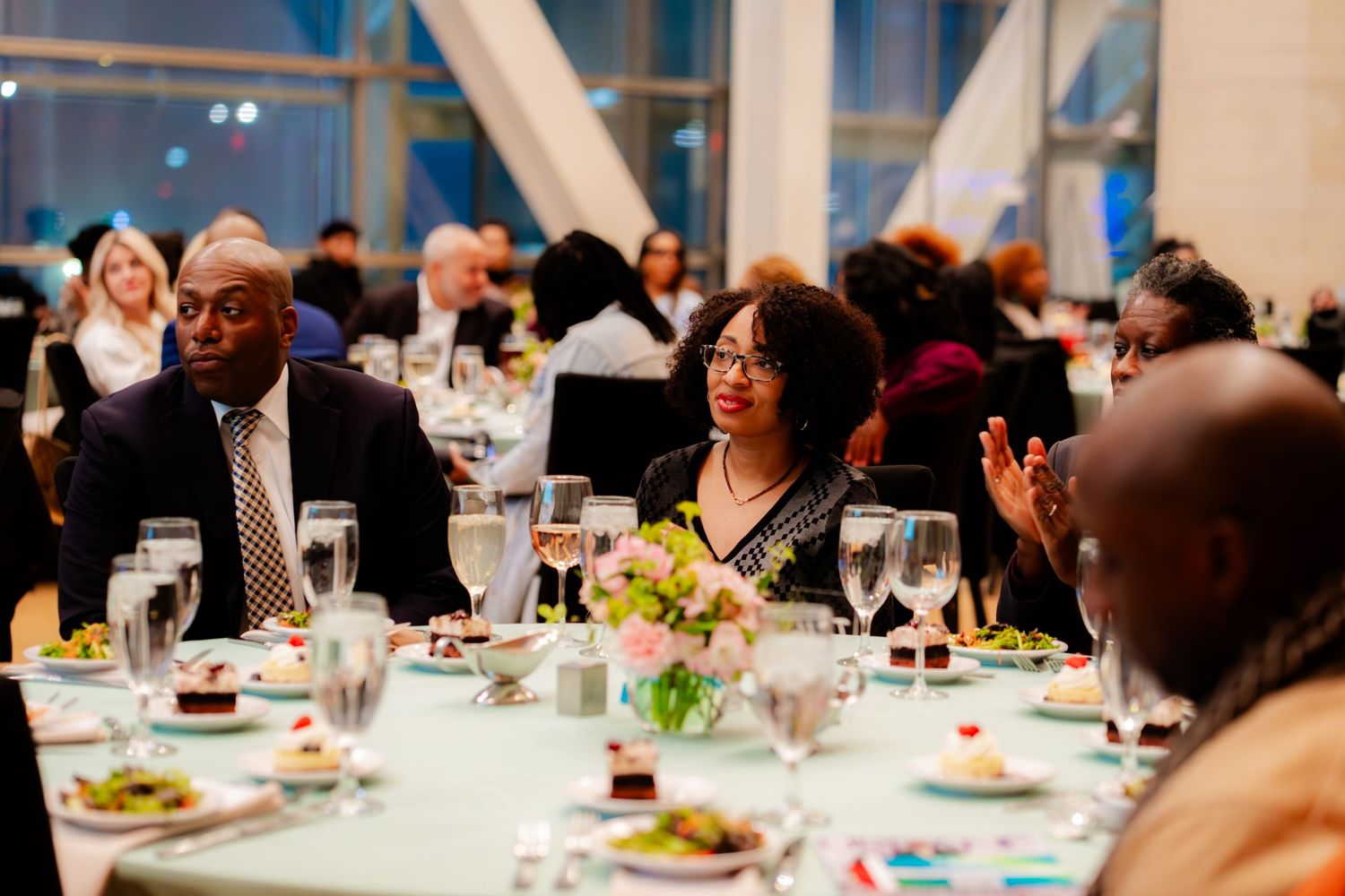 Guests enjoying conversation and dining at an elegant banquet with formal table settings and white linens.