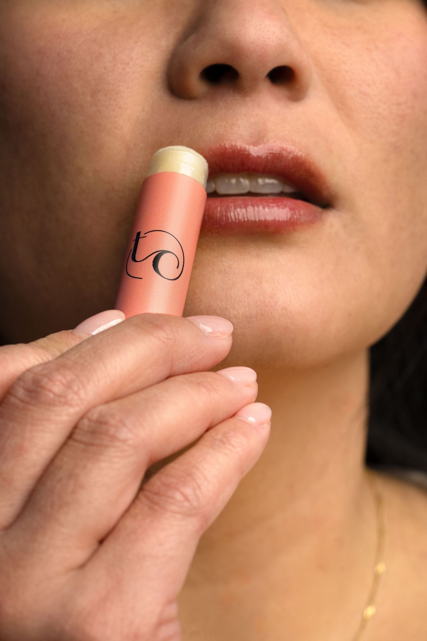 Close-up of hand applying coral-colored lip balm product.