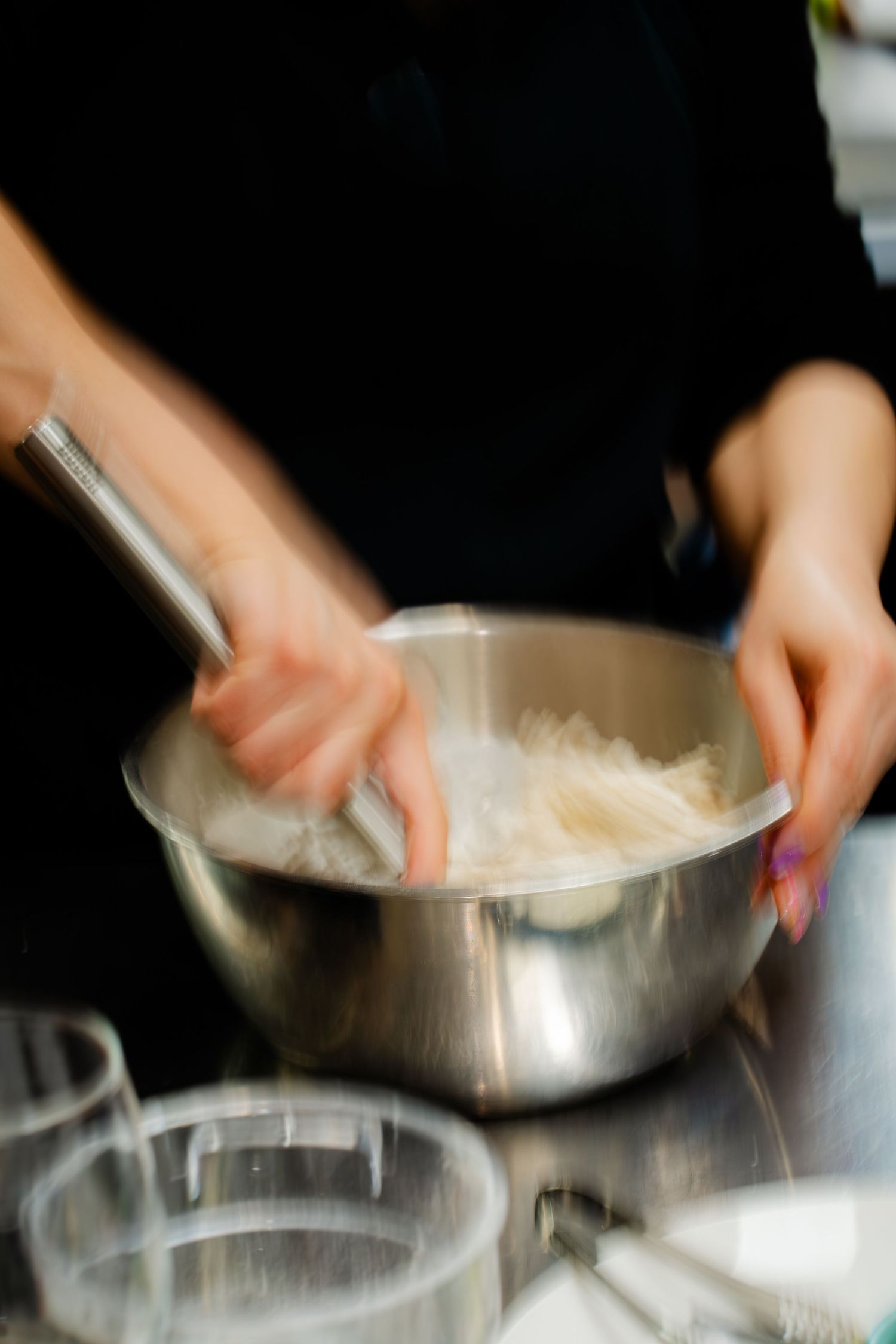 Chef mixing ingredients in a stainless steel bowl on a kitchen counter with blurred motion effect.