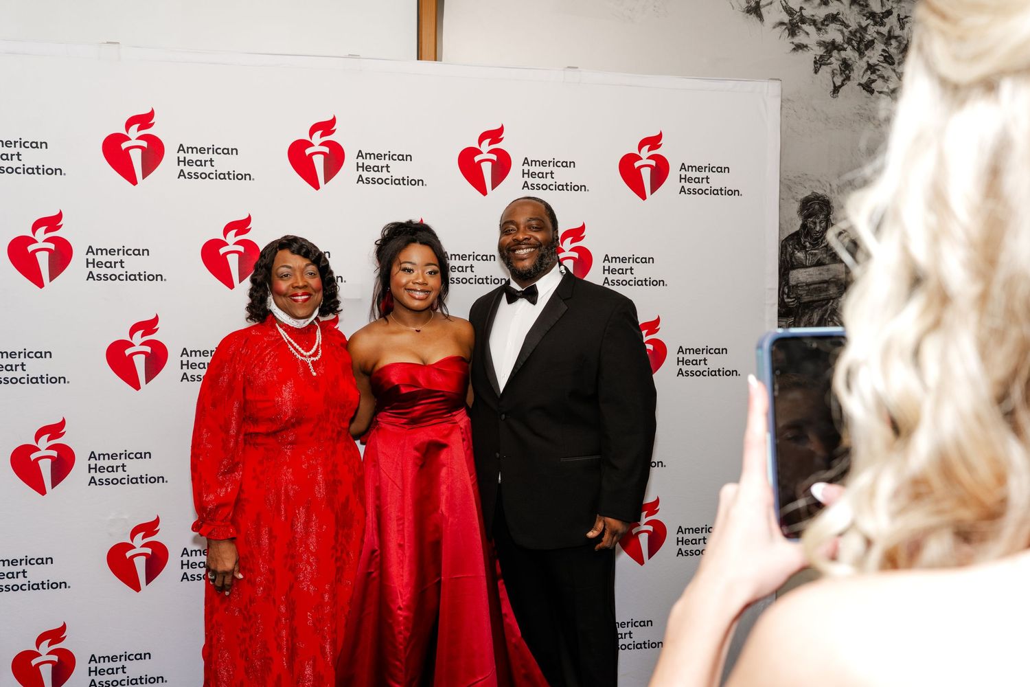 Attendees in formal attire pose against American Heart Association branded backdrop at charity event.