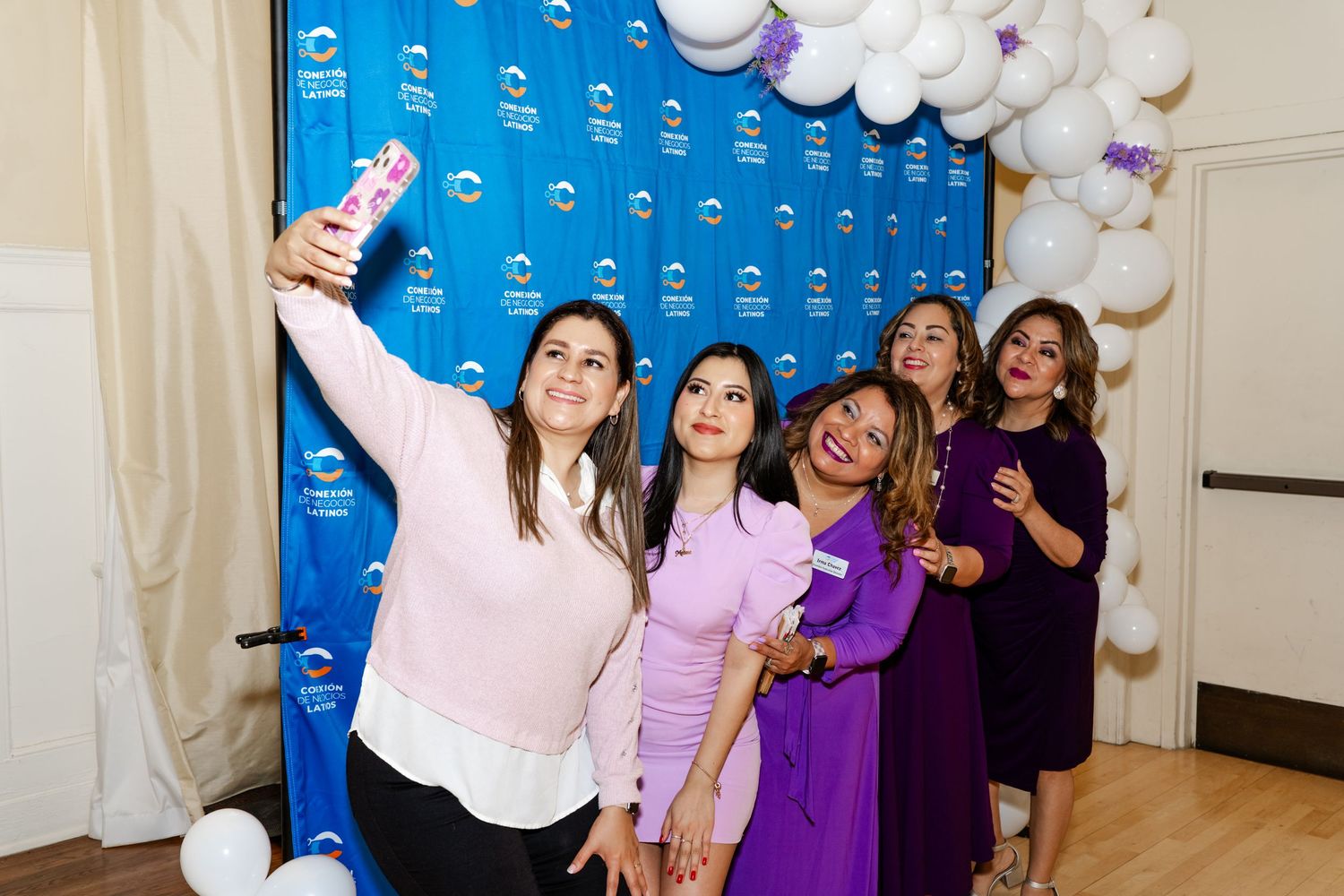 Group celebration with purple and white balloon decorations against blue backdrop.