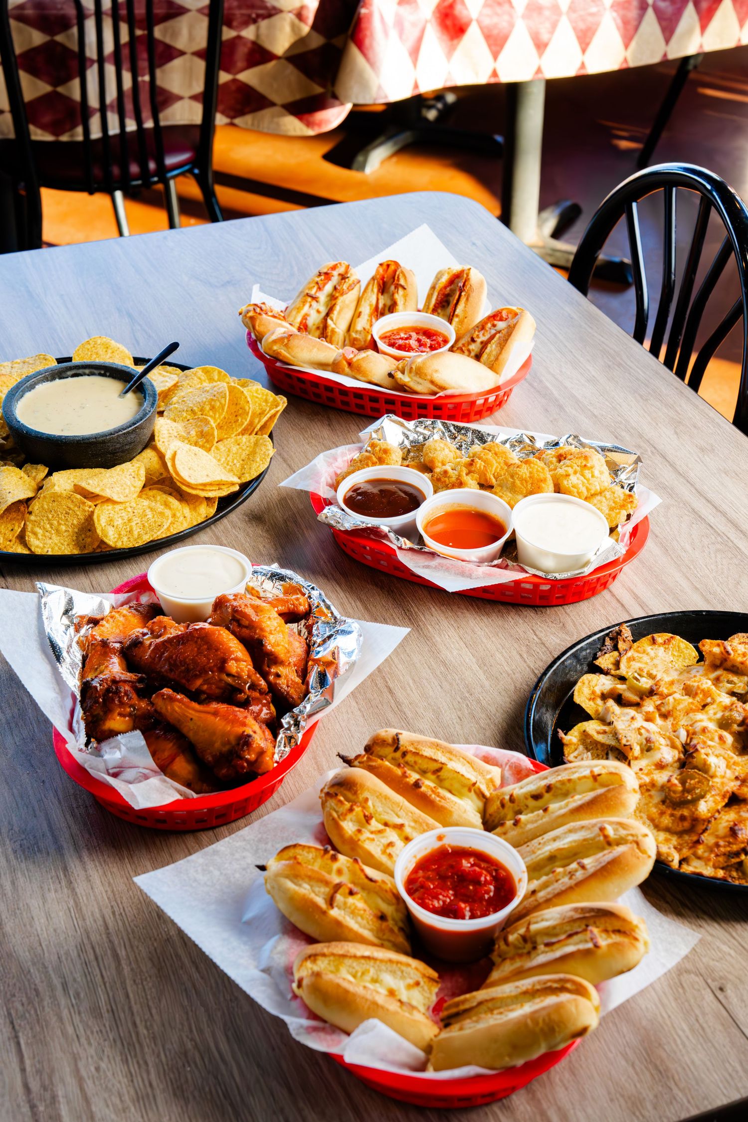 Fast food restaurant table with hot dogs, french fries, chicken wings, and various dipping sauces served in red baskets.