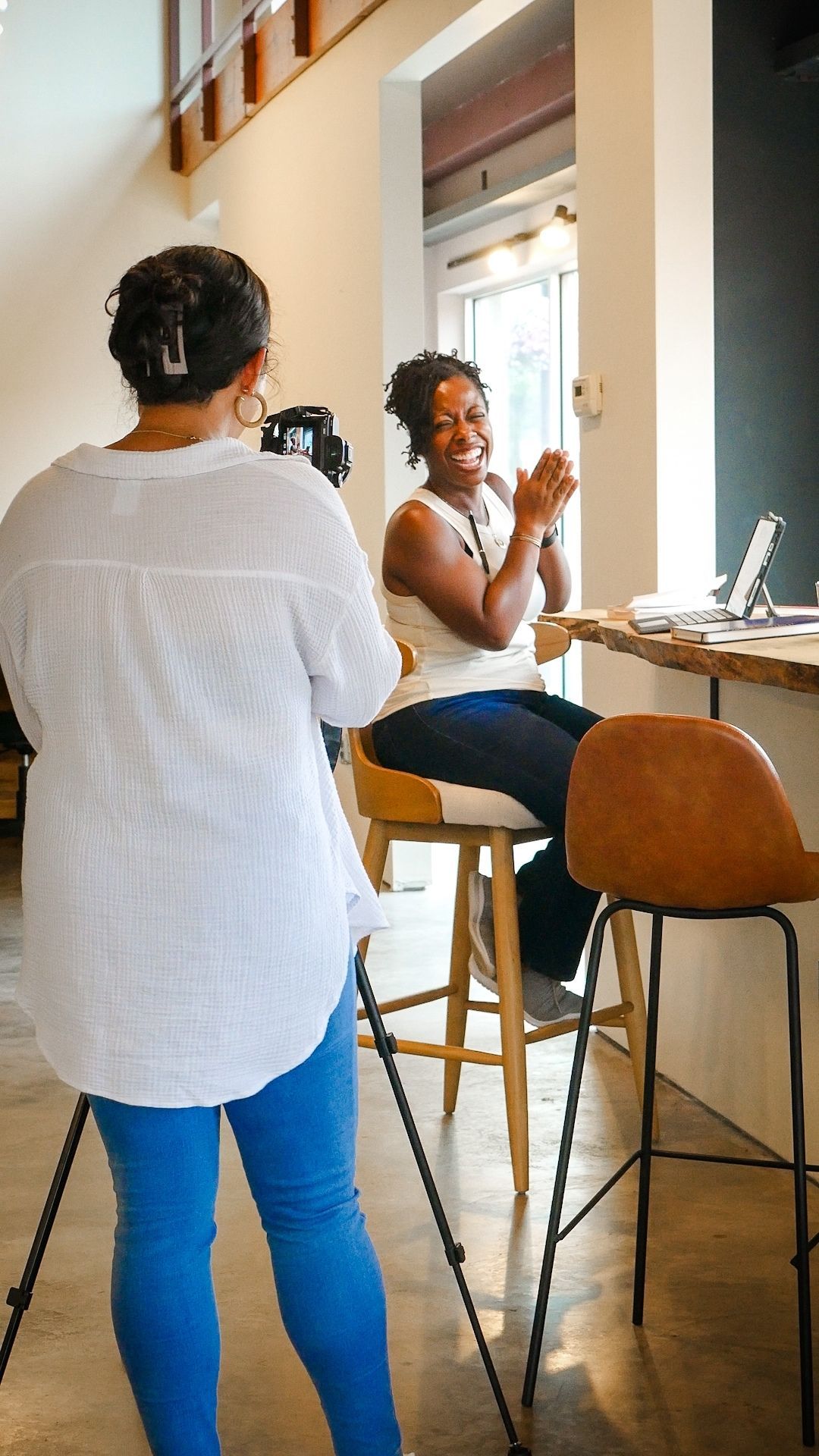 Two people having an animated conversation at a high-top table with a laptop in a bright modern cafe space.