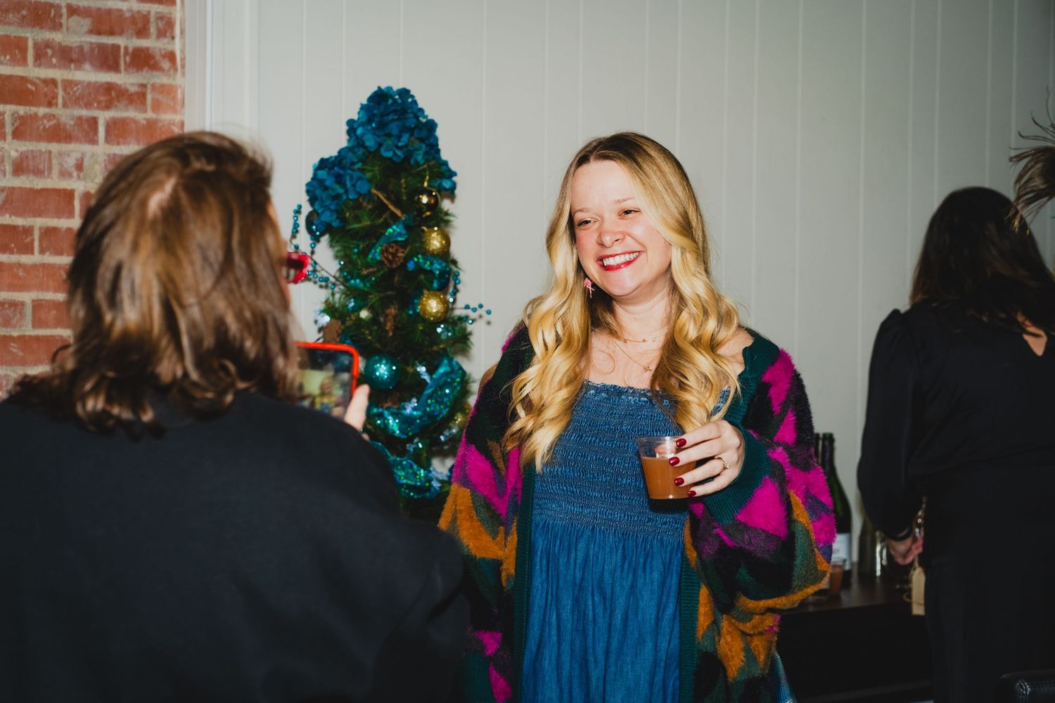 Festive party scene with Christmas tree and guests in formal attire against exposed brick.