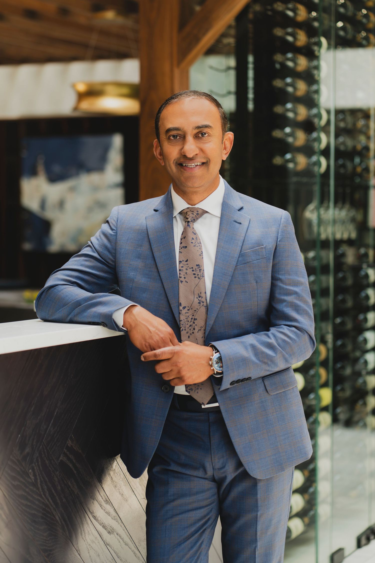 Professional man in blue suit and floral tie smiling confidently in an upscale restaurant setting.