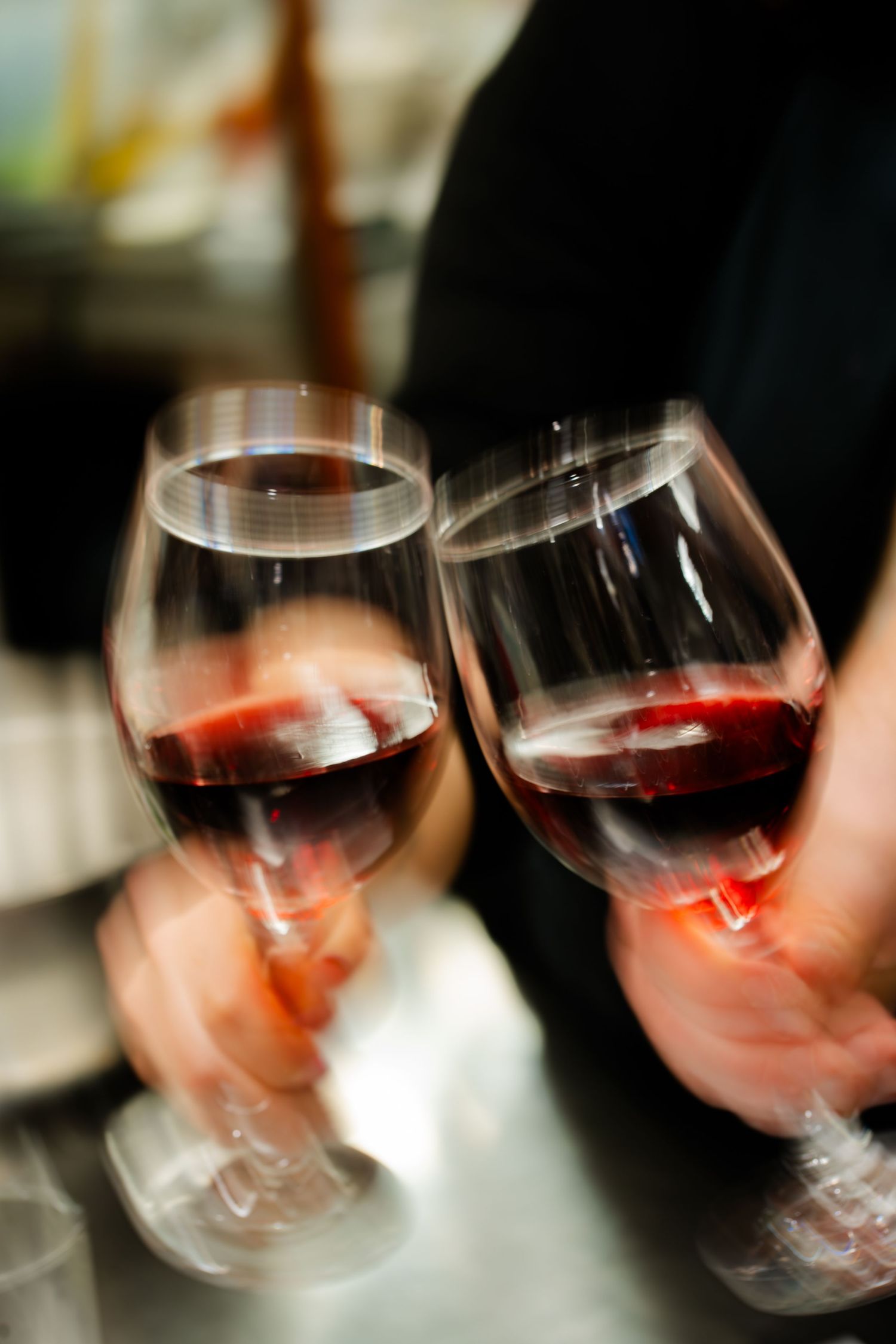 Two hands clinking glasses of red wine in a celebratory toast, captured with motion blur effect.