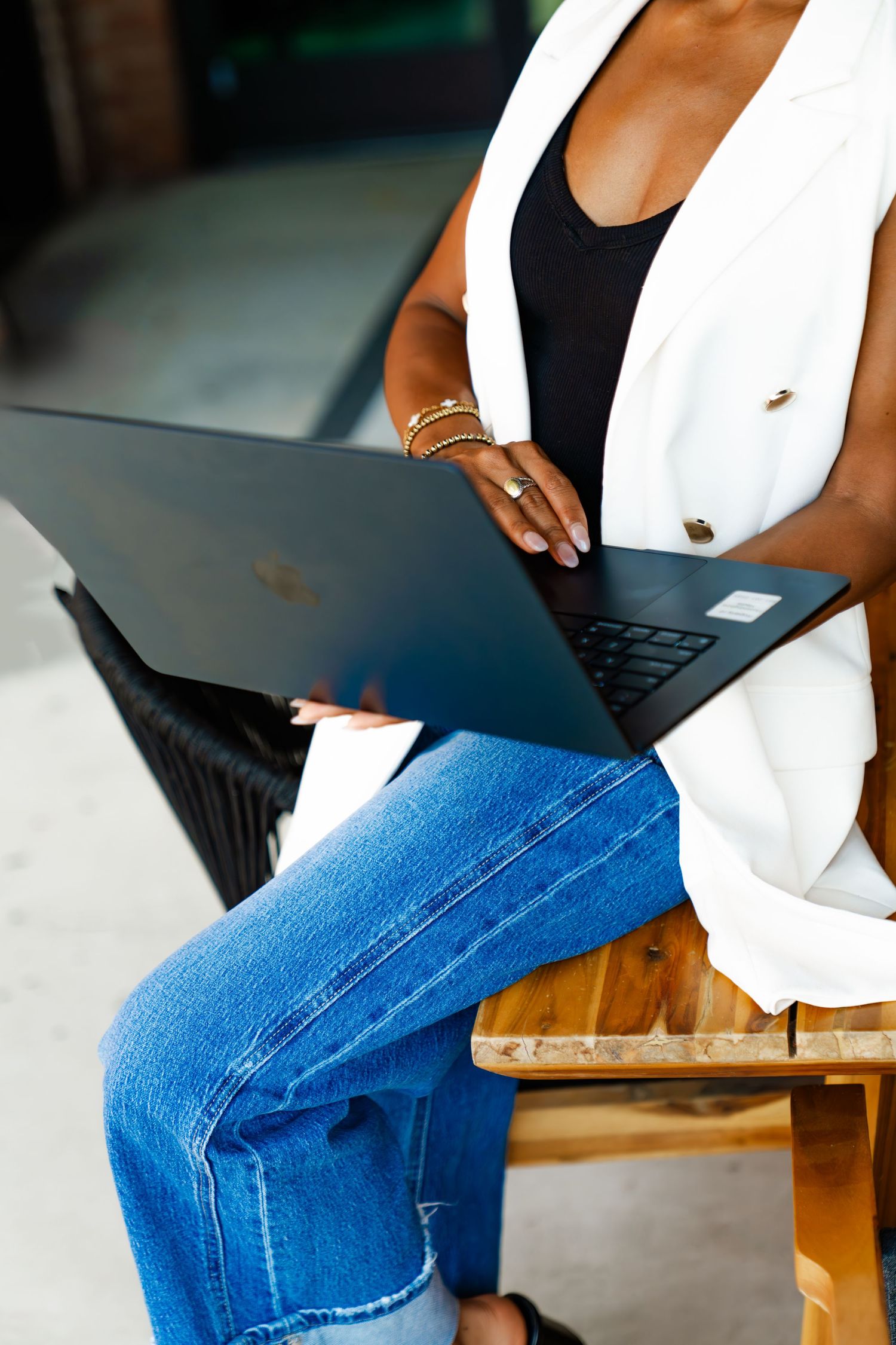 Person wearing white blazer and blue jeans working on laptop computer.