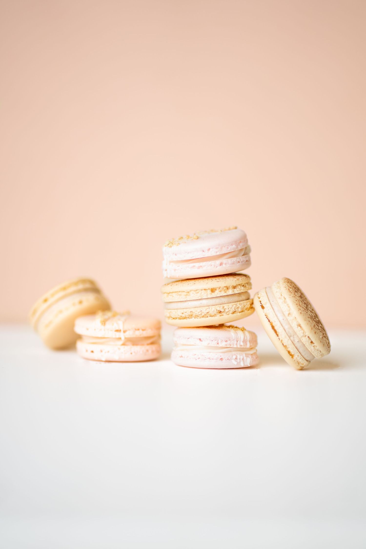 Delicate pink macarons stacked and arranged on white surface against blush background.