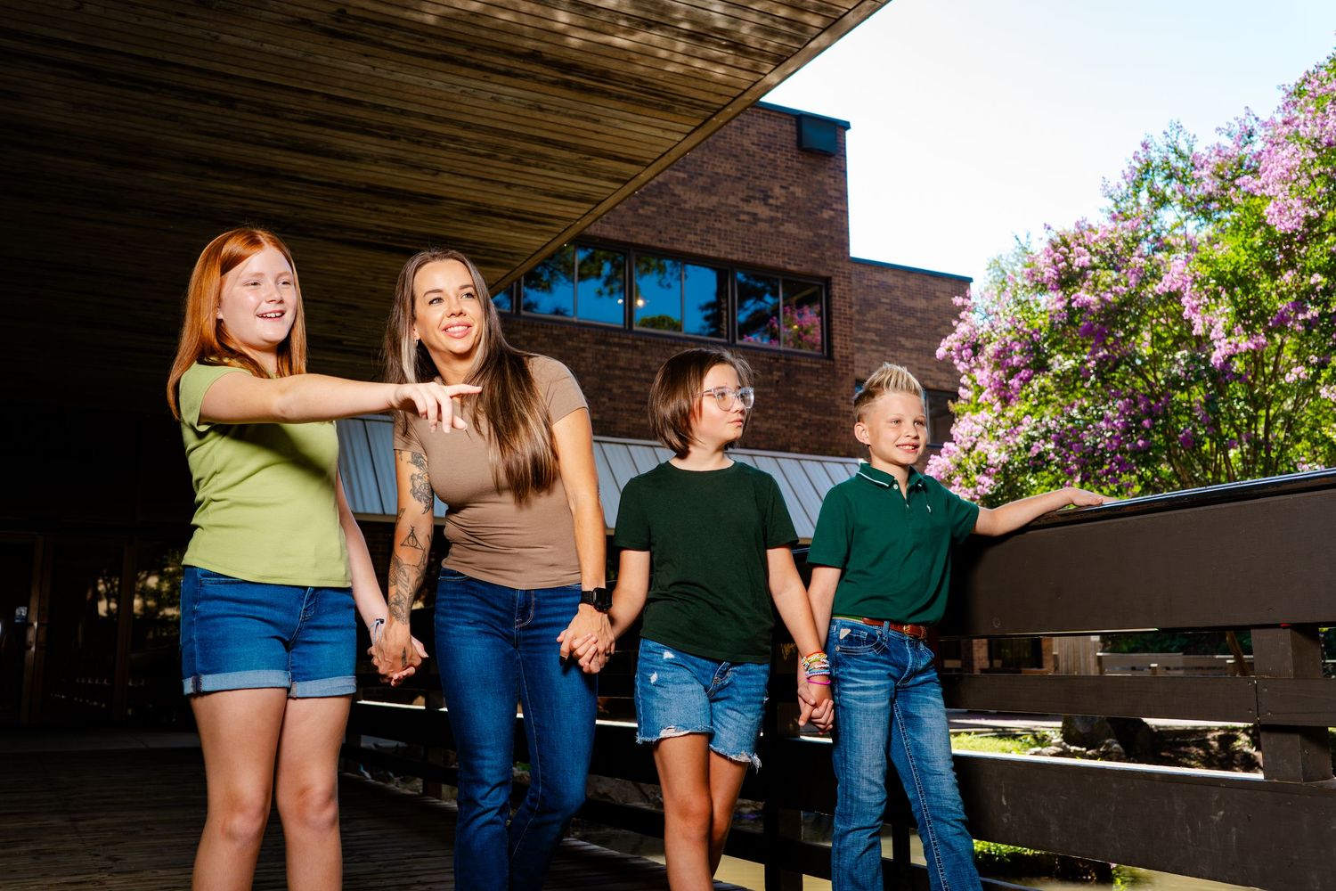 People walking together outdoors near flowering bushes and wooden structures.