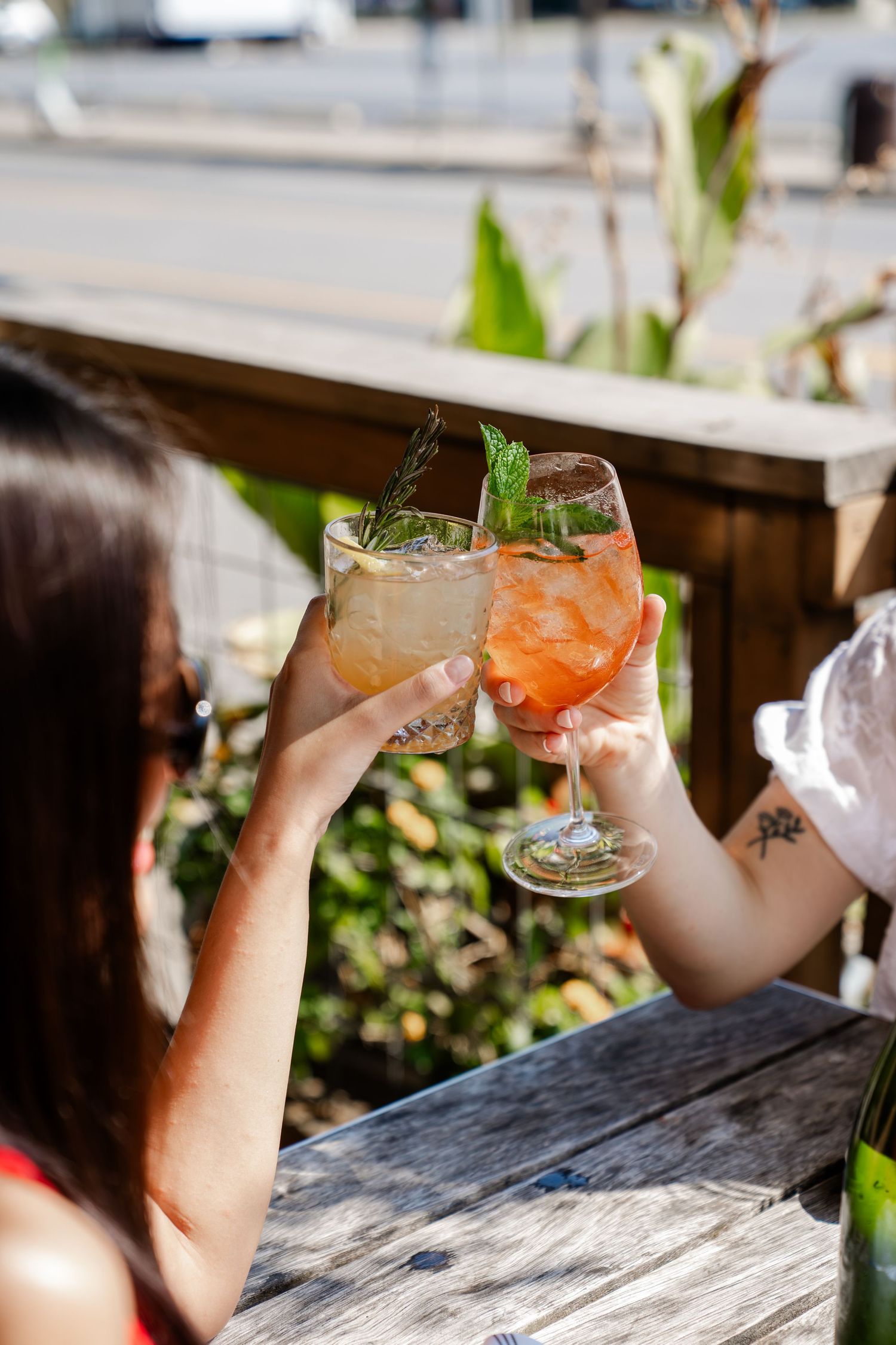 Two people toasting with colorful cocktails garnished with mint at an outdoor patio.