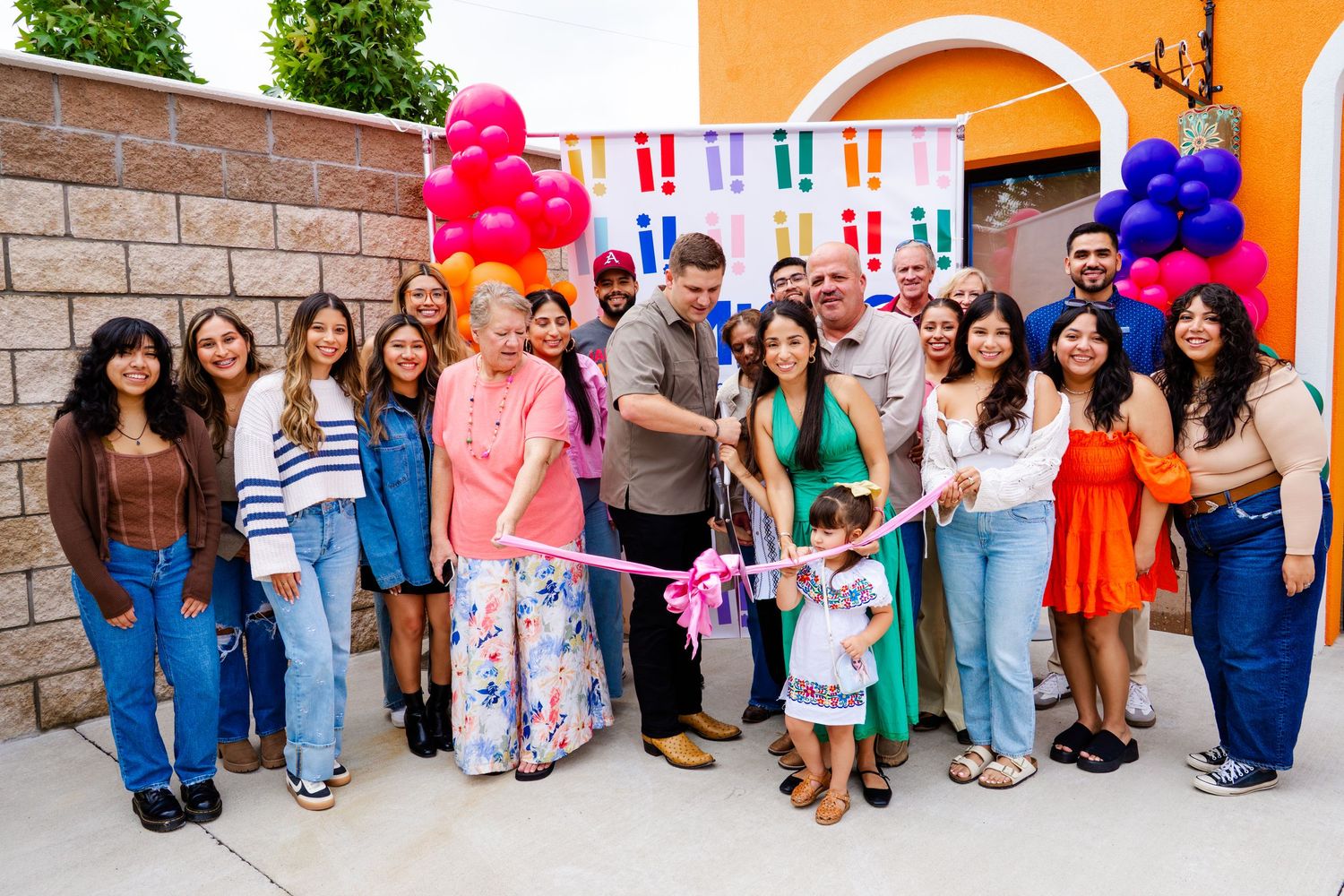Large group gathered outside a colorful building for a celebratory event with balloons and decorations.