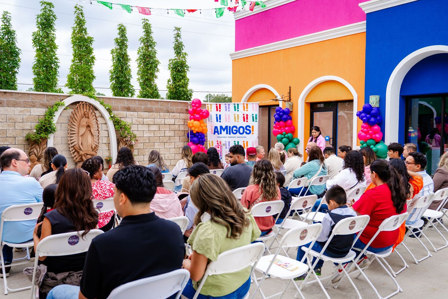 Outdoor event with colorful banners and white chairs set up under bright blue sky.