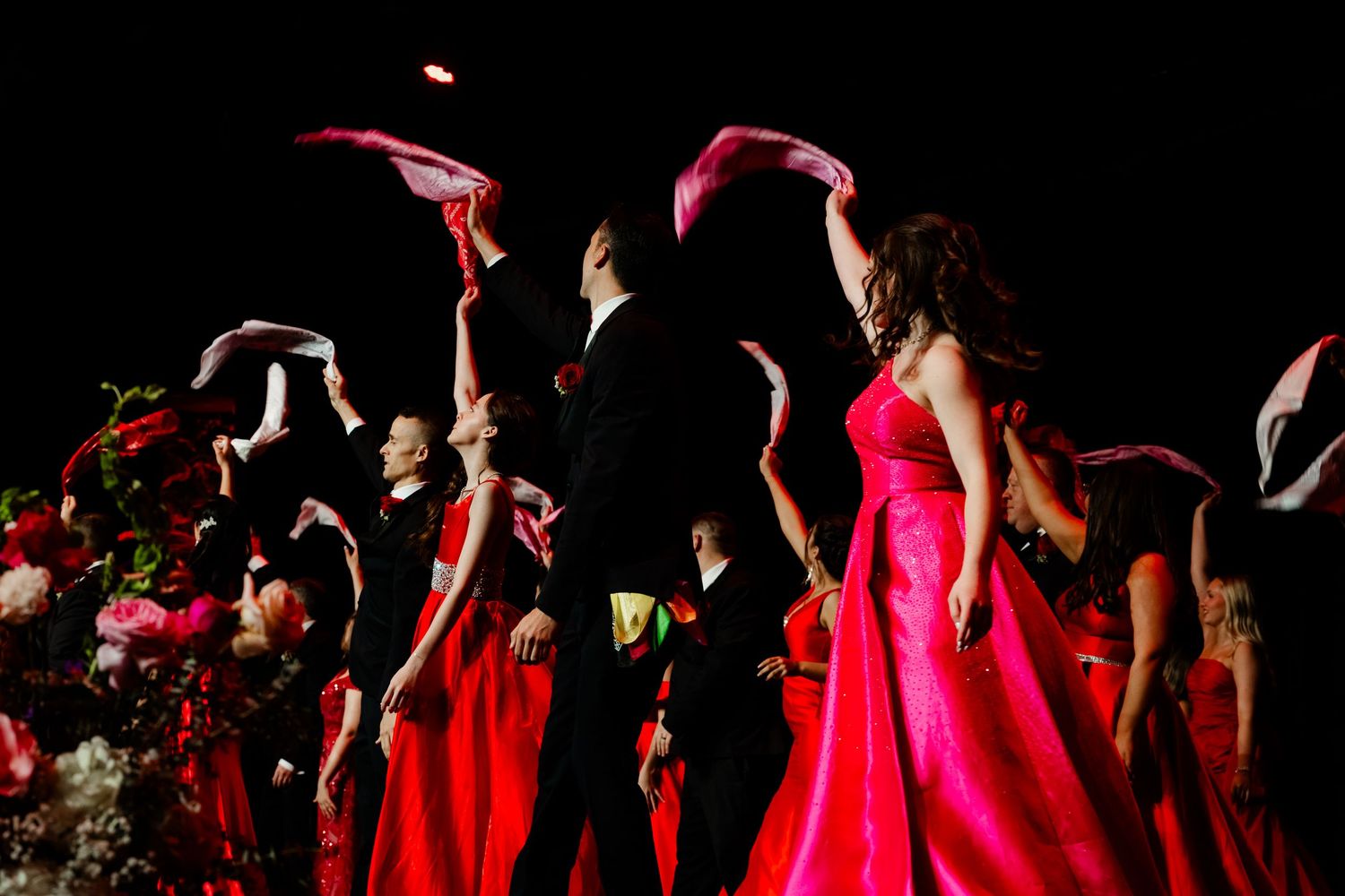 Silhouettes of performers in formal wear and gowns on darkened stage.