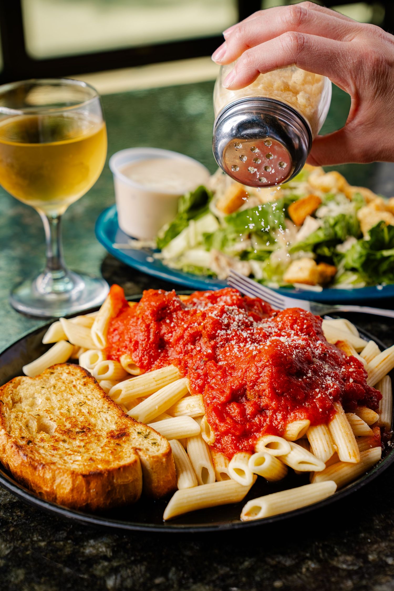Pasta with red marinara sauce served with garlic bread and salad alongside white wine.