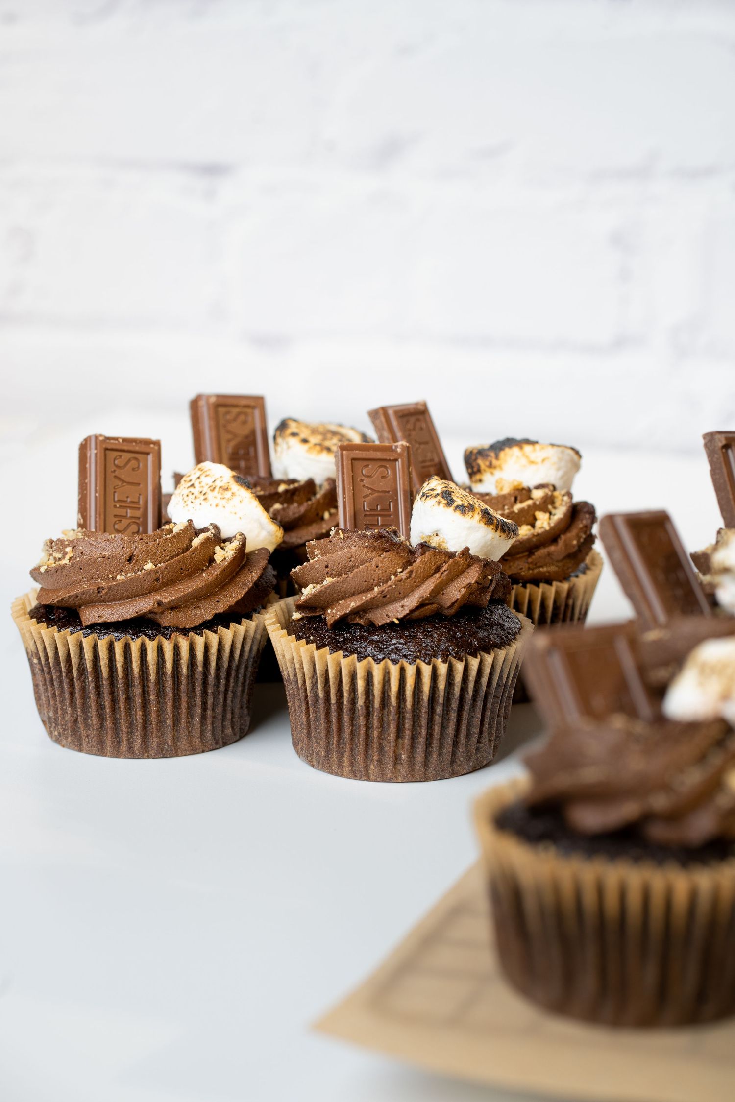 Chocolate cupcakes topped with frosting and chocolate bar pieces on a light surface.