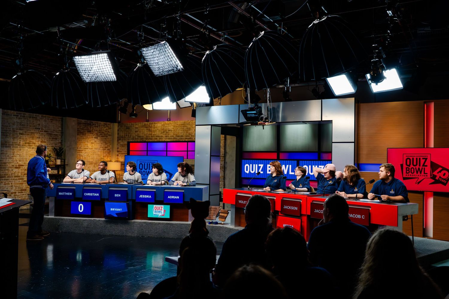 Television studio with red and blue lit contestant stations and audience seating.