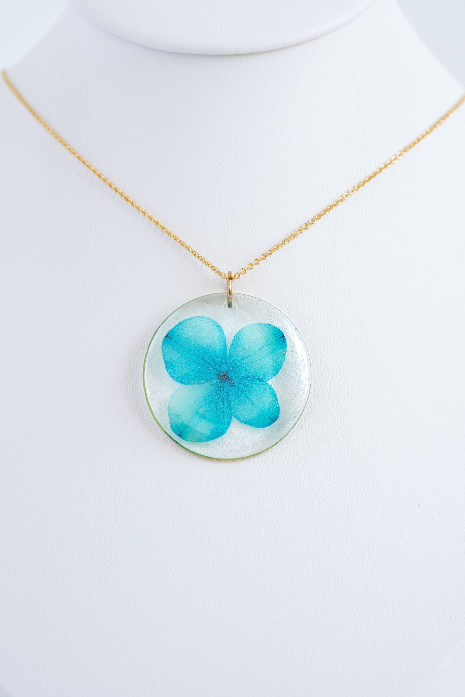 Delicate blue flower preserved in clear resin pendant on gold chain.
