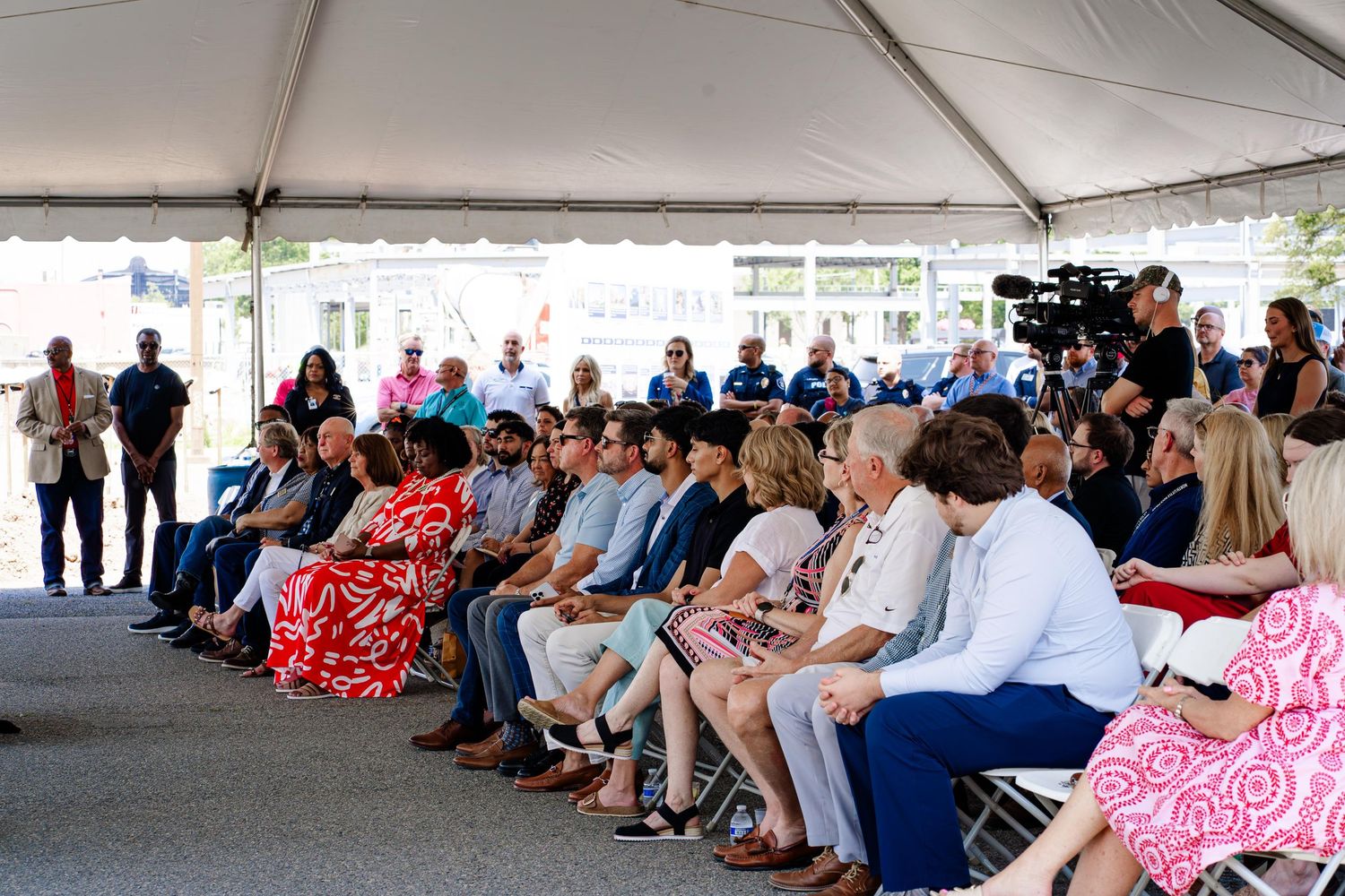 Audience members seated in rows under large white event tent during presentation.