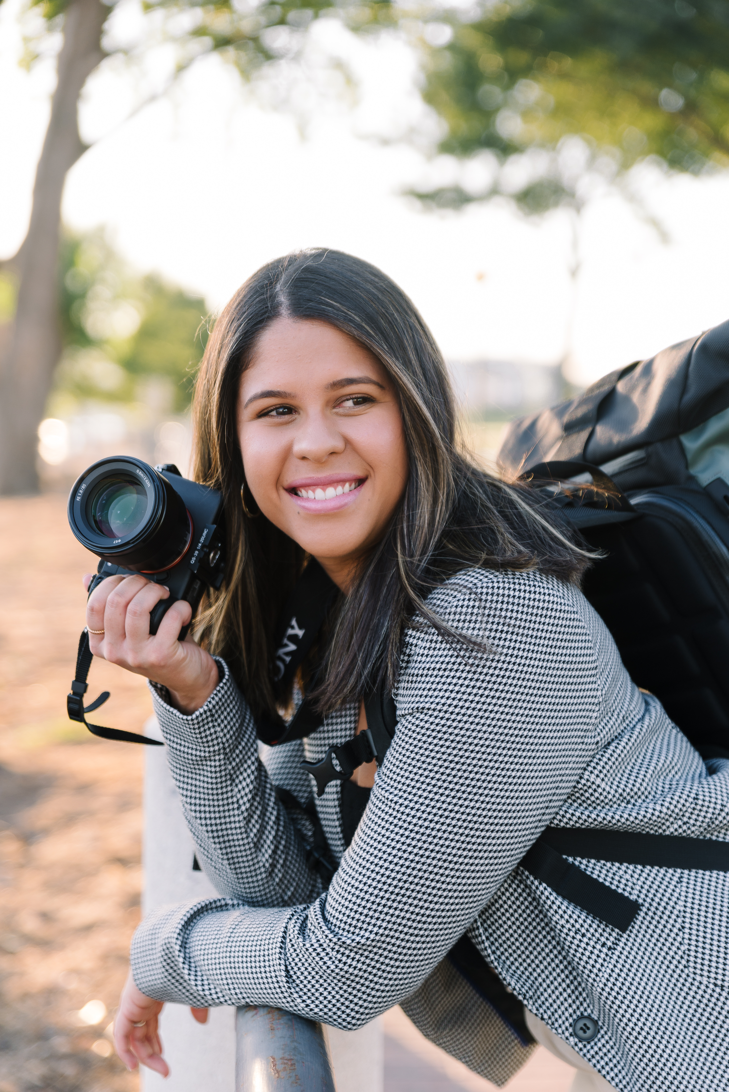 A photographer in striped sweater holds camera equipment outdoors.