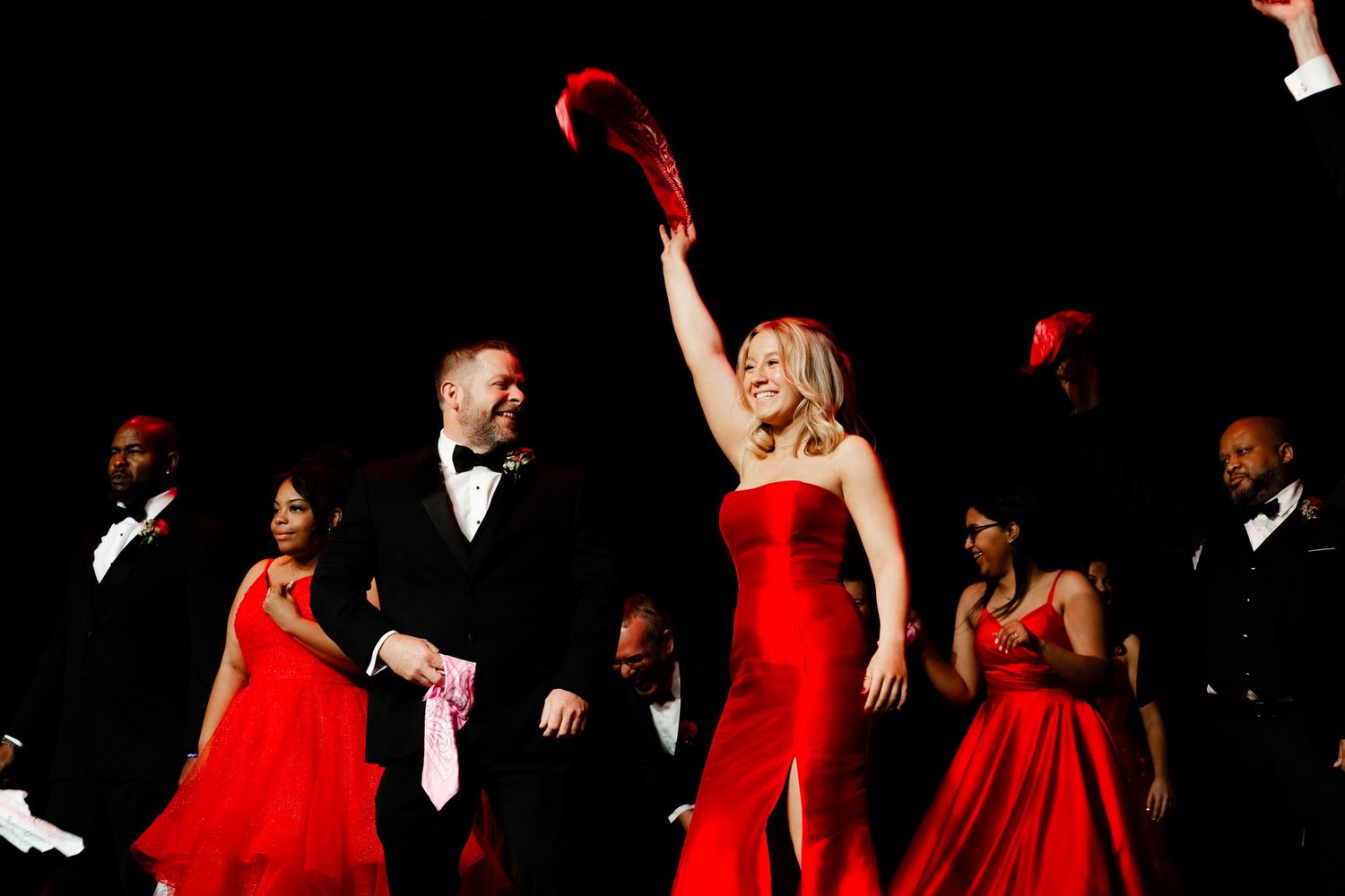 Performers in red gowns and formal attire on stage during charity gala show.