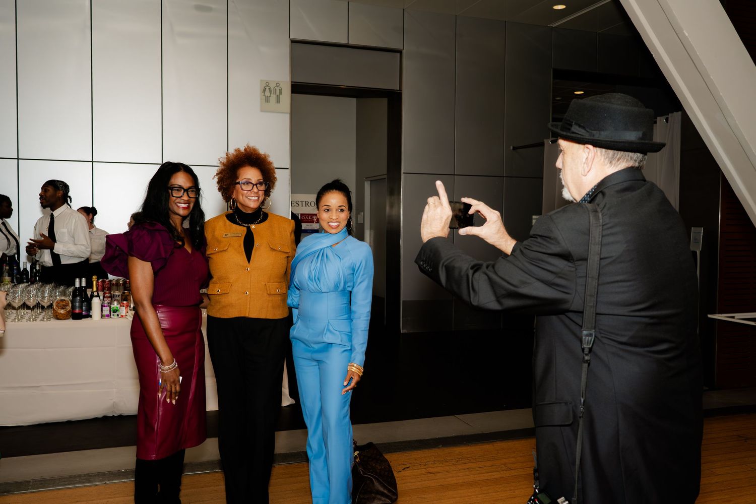 A photographer captures three women posing in colorful outfits at an indoor event.