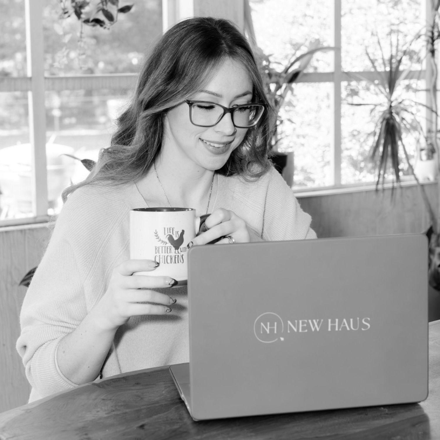 Black and white photo of someone wearing glasses working on a New Haus laptop while holding a coffee cup.