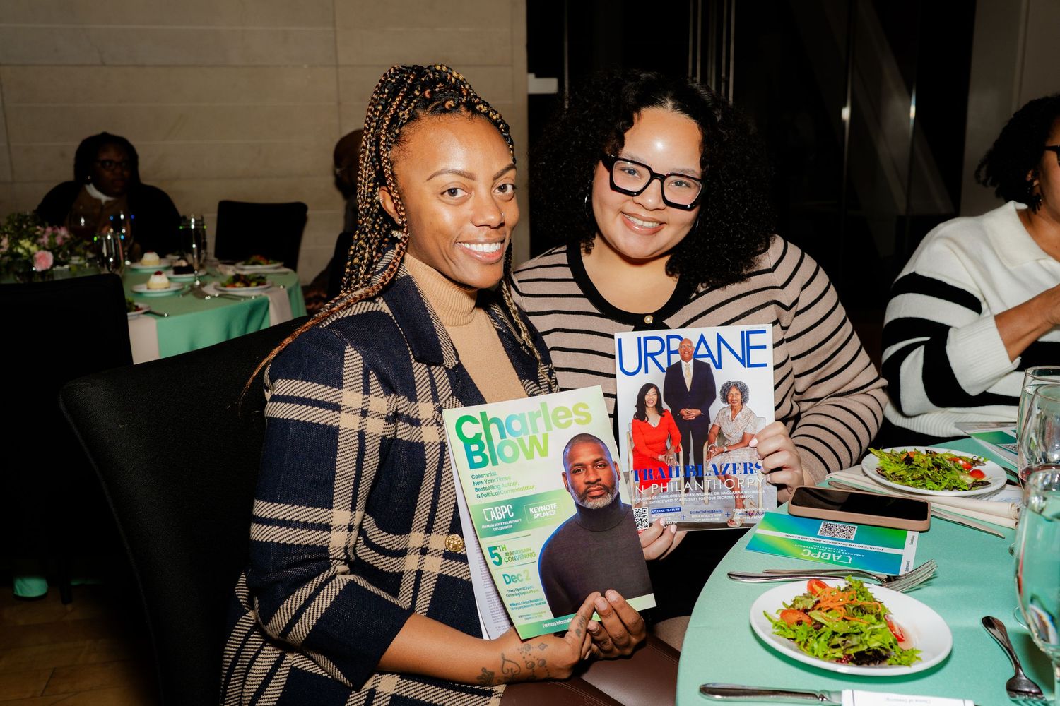 Two attendees share magazines while seated at a table during an event.