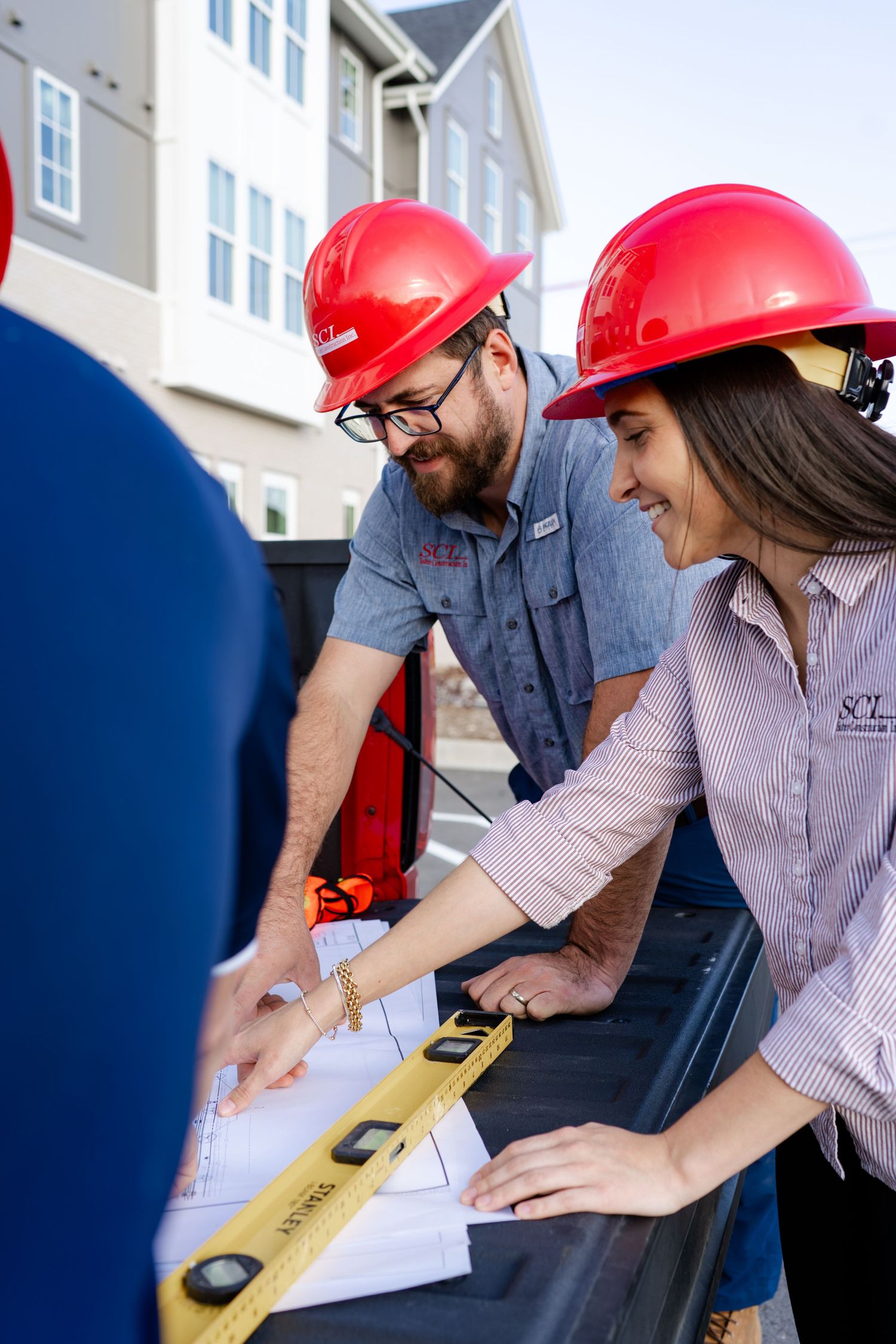 Construction professionals examine building plans while wearing safety gear and using measuring tools.