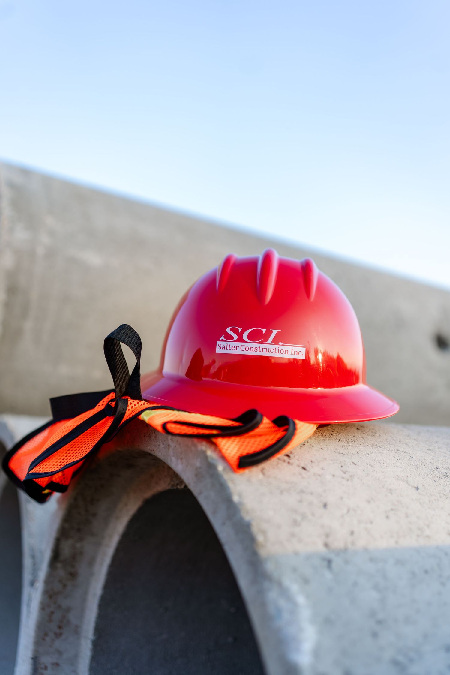 Red hard hat with safety straps rests on concrete surface in construction setting.