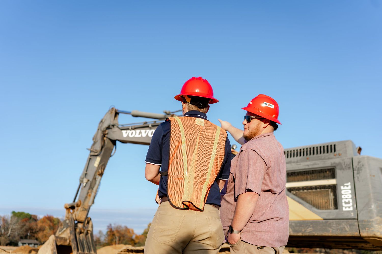 Construction team surveys outdoor site progress against blue sky background.
