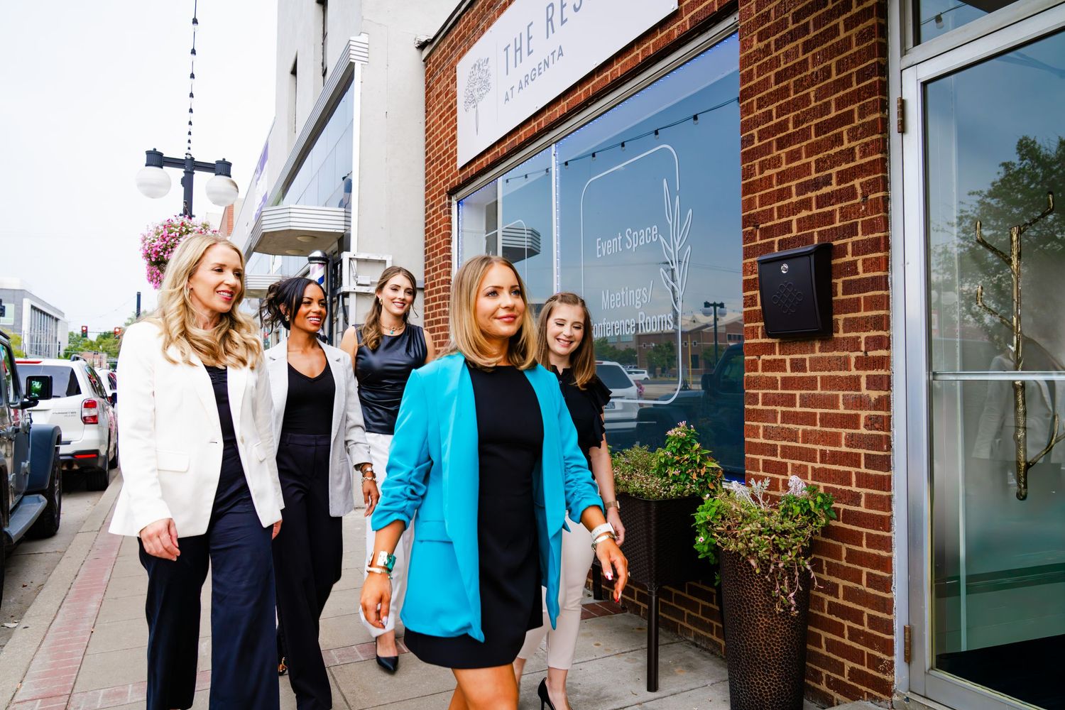 Professional women in business attire walking together outside a brick office building.