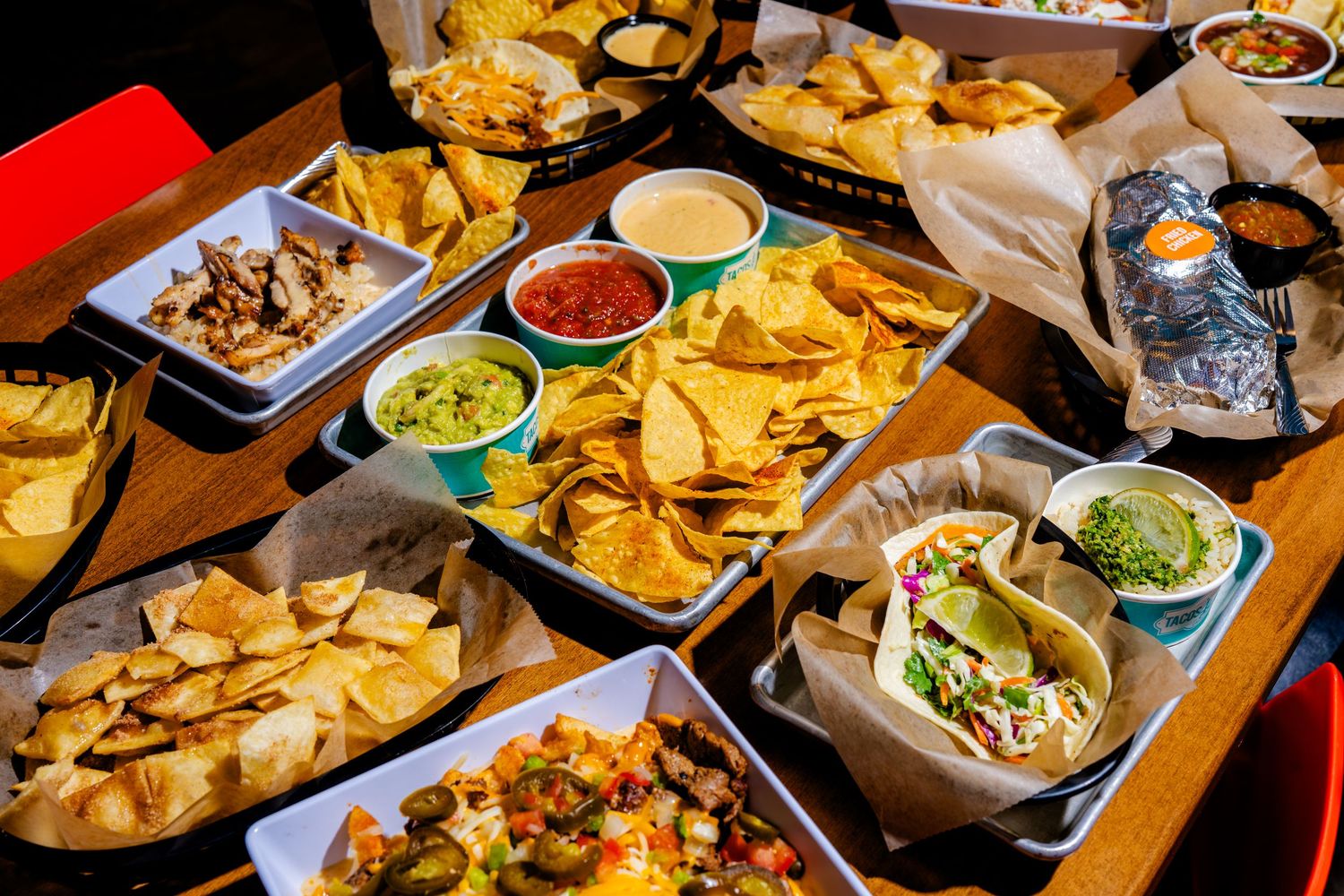 Mexican restaurant spread with tortilla chips, guacamole, salsa, and various dishes on wooden table.