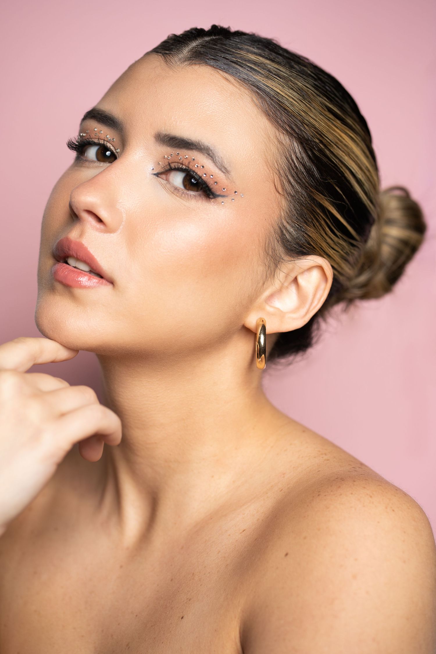 Beauty portrait with sleek updo and natural makeup against pink background.