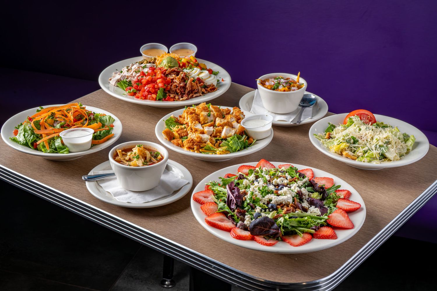 Restaurant plates with colorful salads and entrees arranged on purple backdrop.