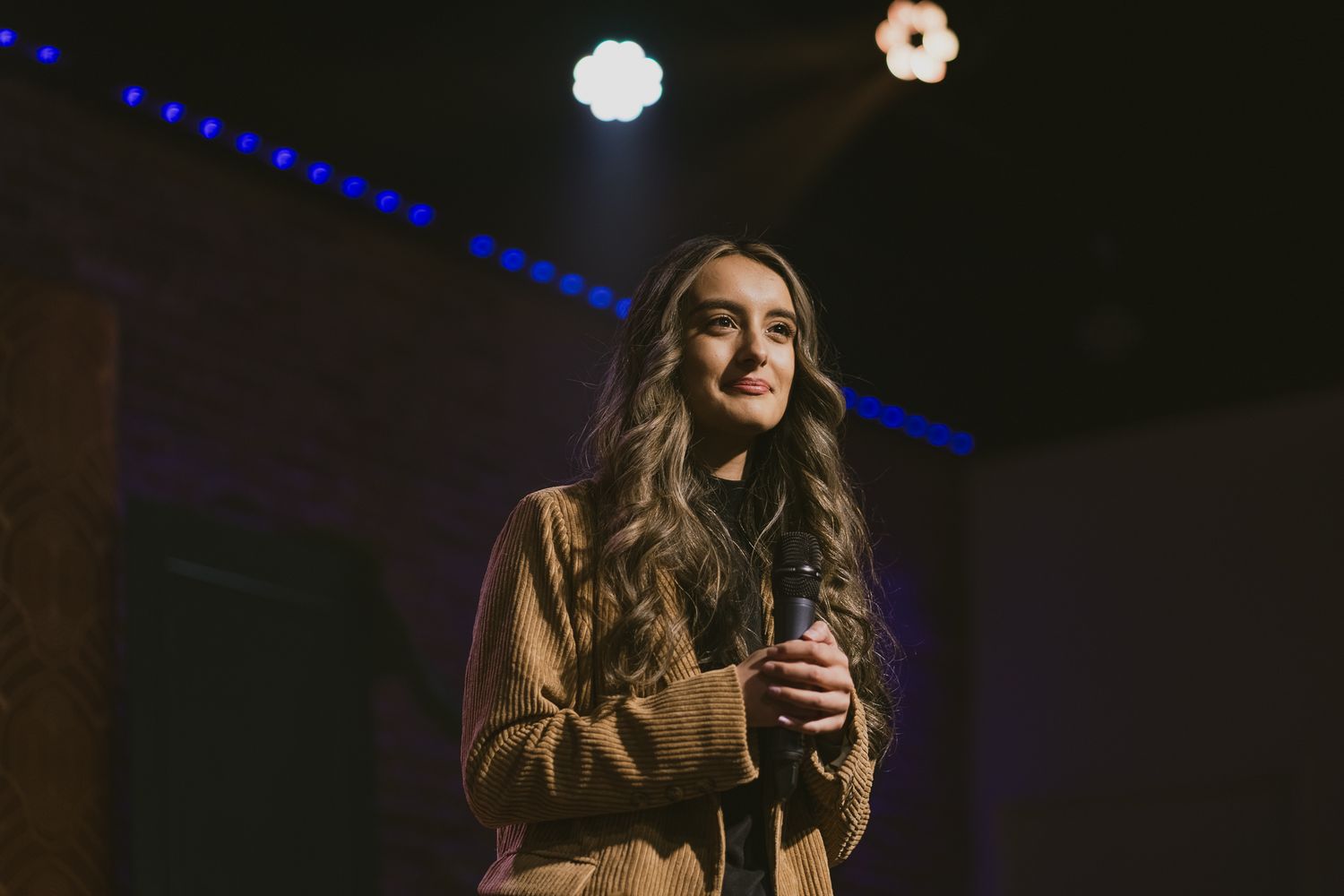 A performer on stage in a dark venue with dramatic blue lighting.